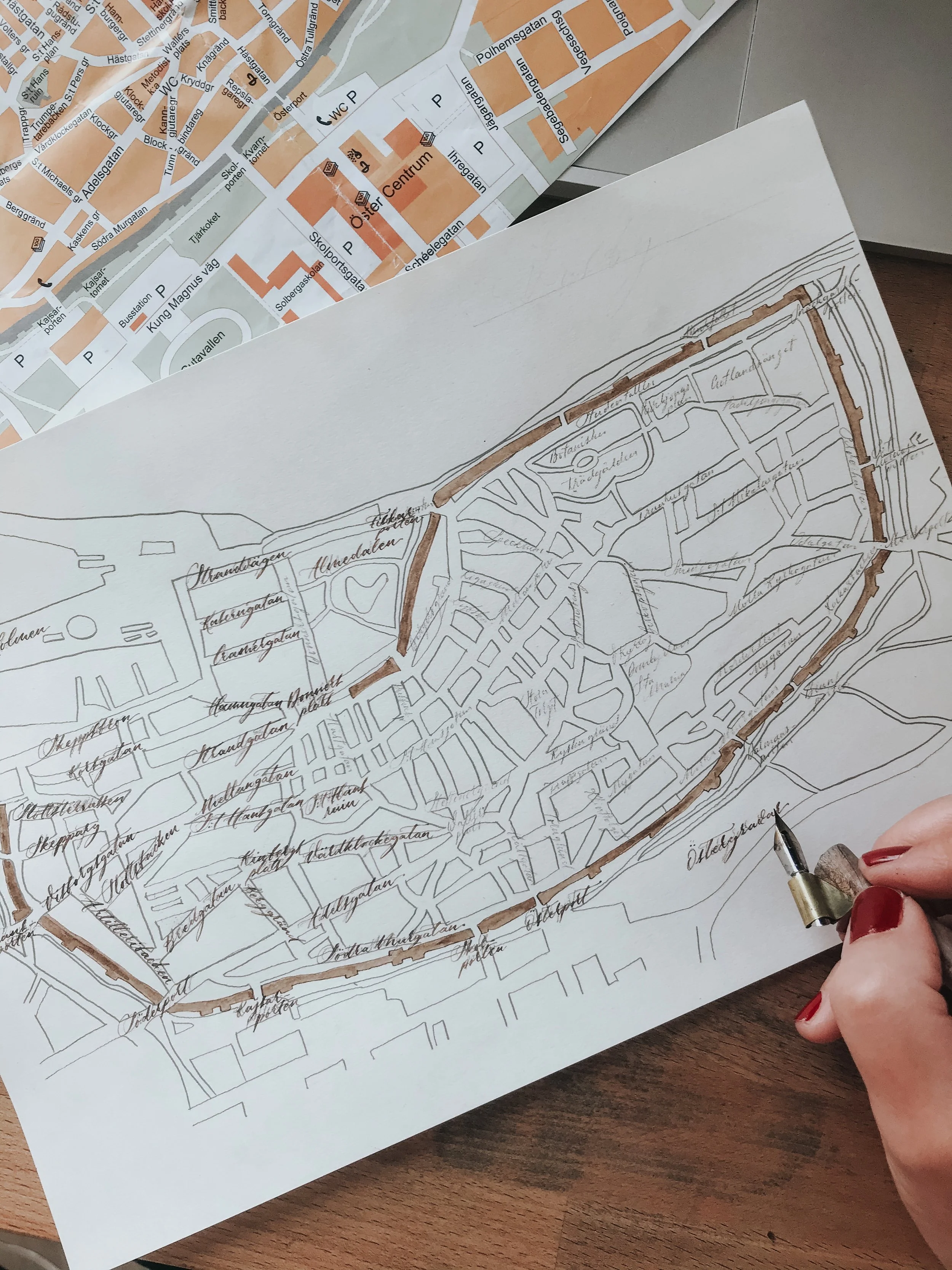 Hand-drawn map of Visby, Sweden, and a woman's hand holding a calligraphy pen
