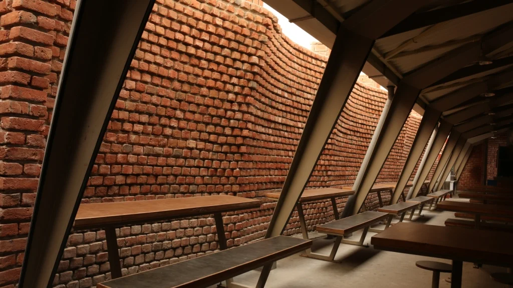  The steel columns are separated from the corrugated sheet roofing by a curved brick wall with a smartly positioned skylight that imparts natural light inside to give wings to a more stress-free environment in the cafeteria. This was contrived to pro