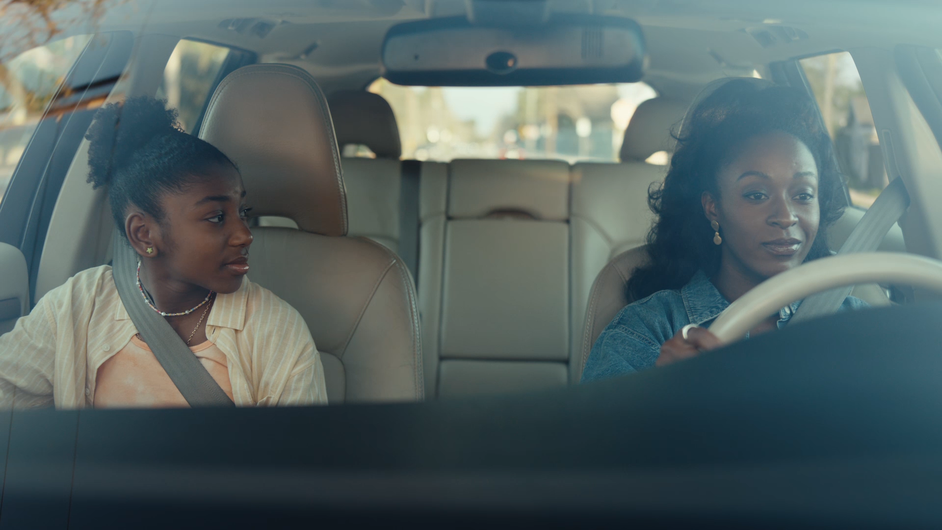 An African American woman driving a car with a young girl sitting in the passenger seat looking at her.