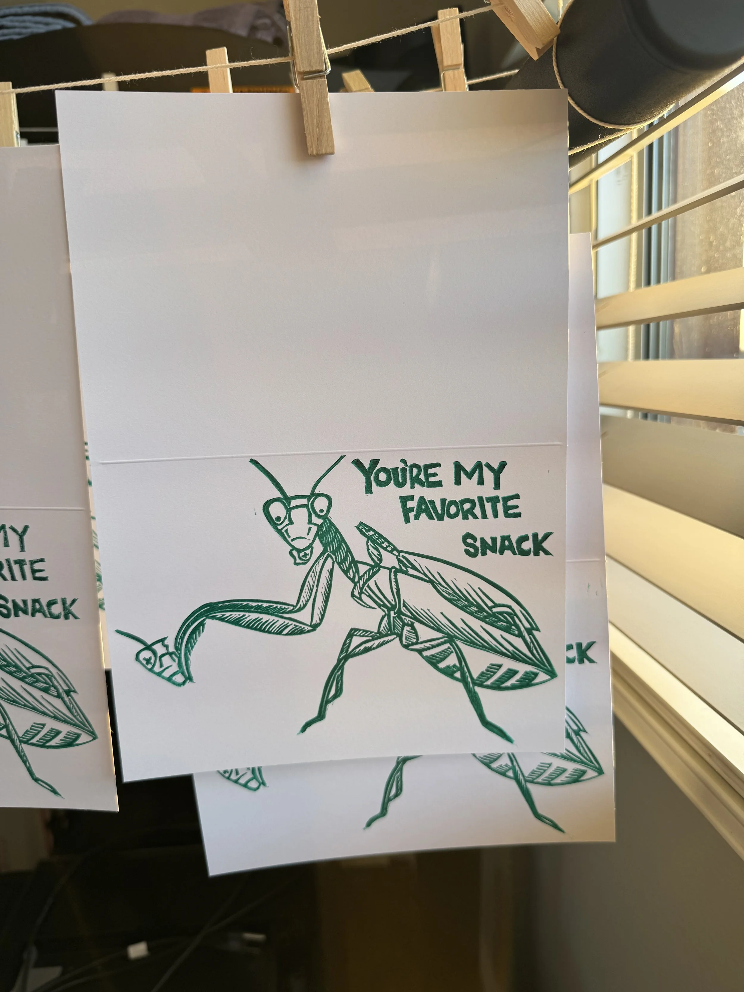 A green linoprint of a female praying mantis with a decapitated male on her back while she eats a portion of the head in her front claws