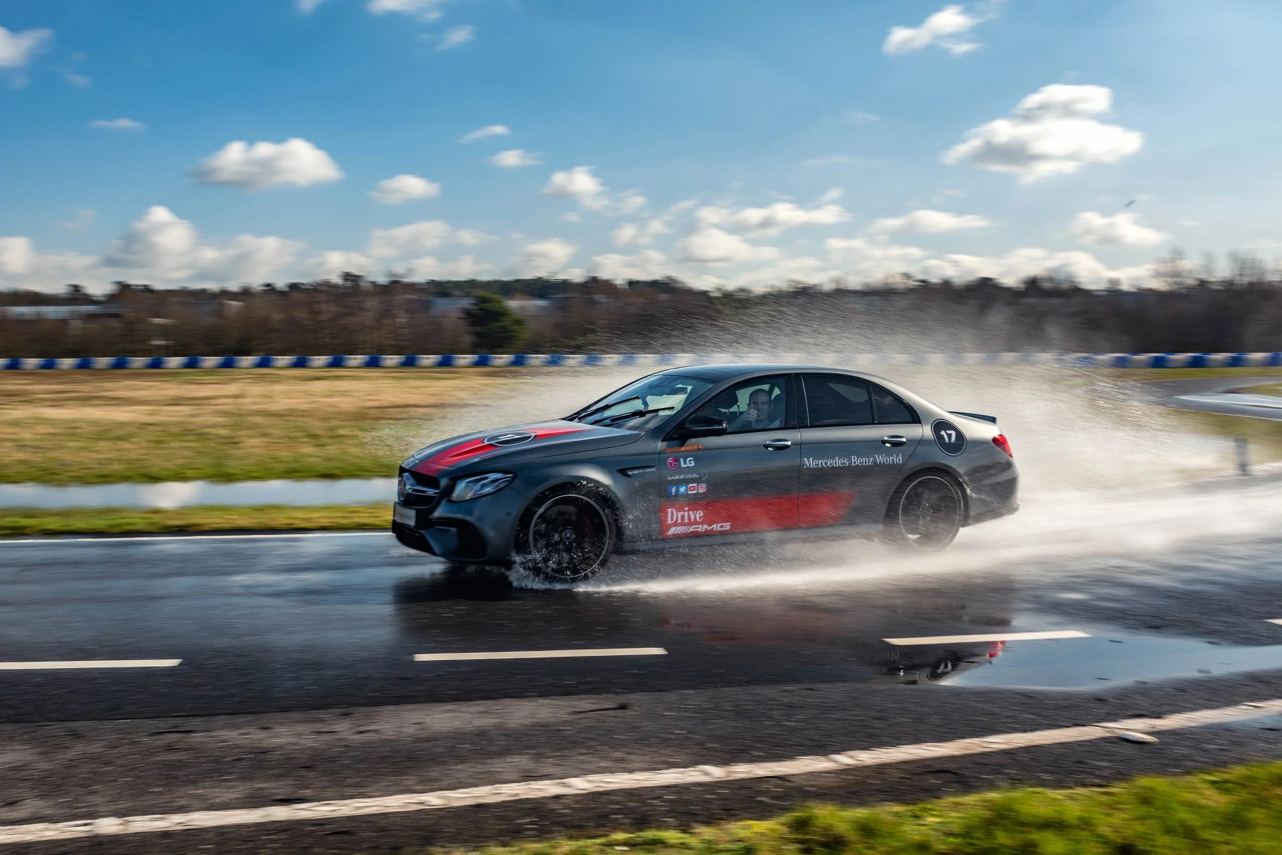 Mercedes-AMG E-Class side-on at speed on the wet Mercedes-Benz World circuit with the driver visible