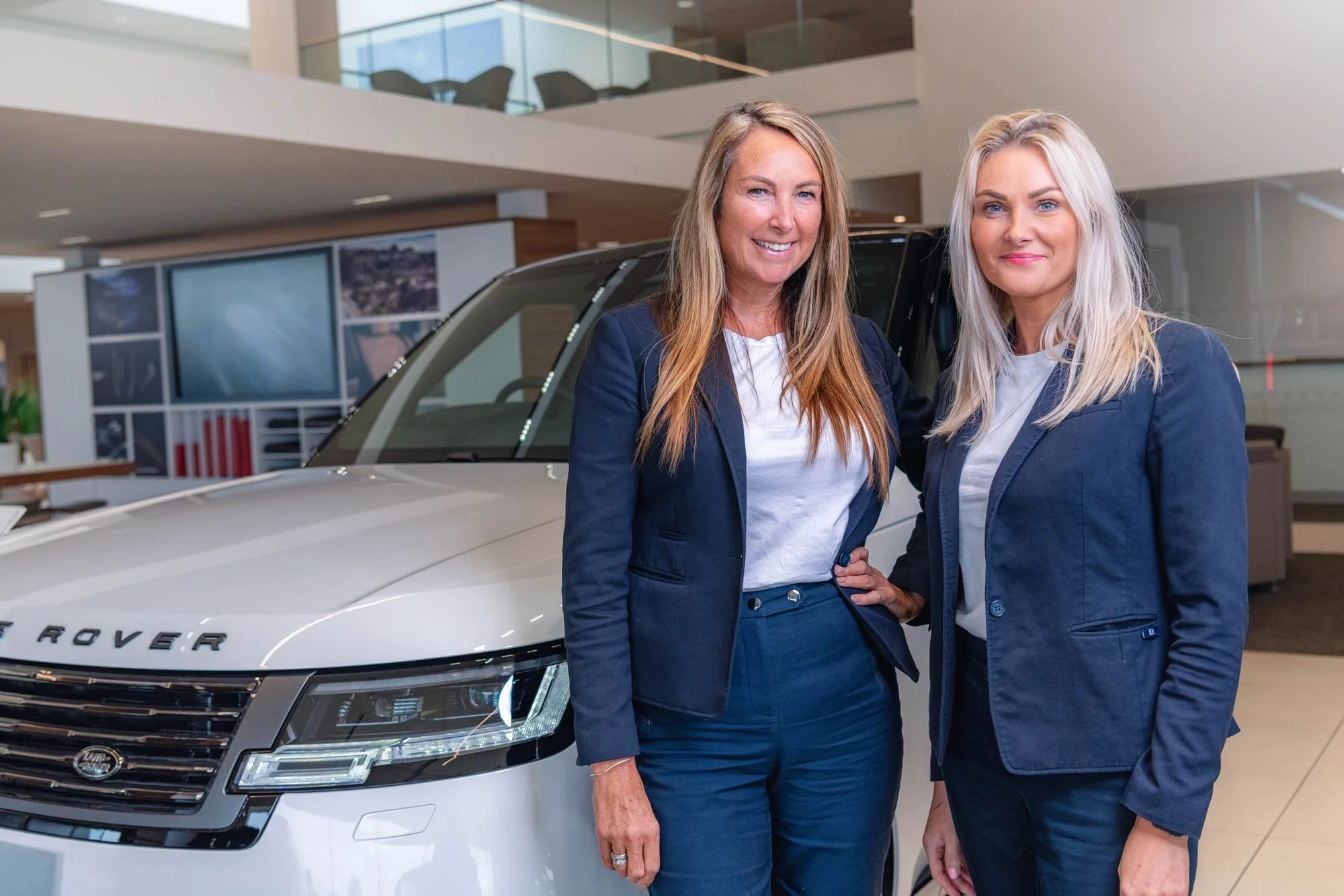 Professional portrait of two female team members in a luxury Range Rover dealership showroom – dealership team photography