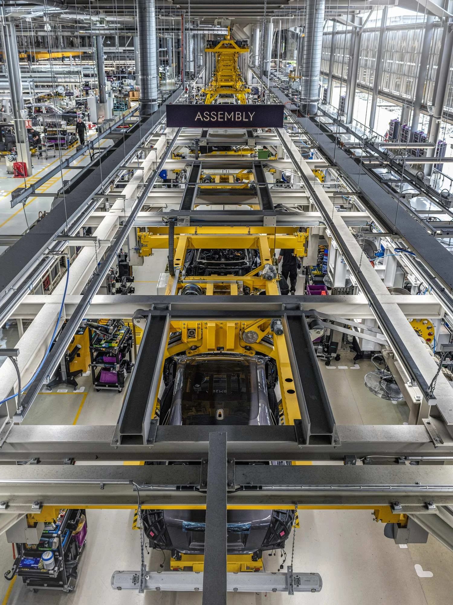 Wide view of busy automotive assembly line with vehicles on robotic arms – industrial manufacturing photography London