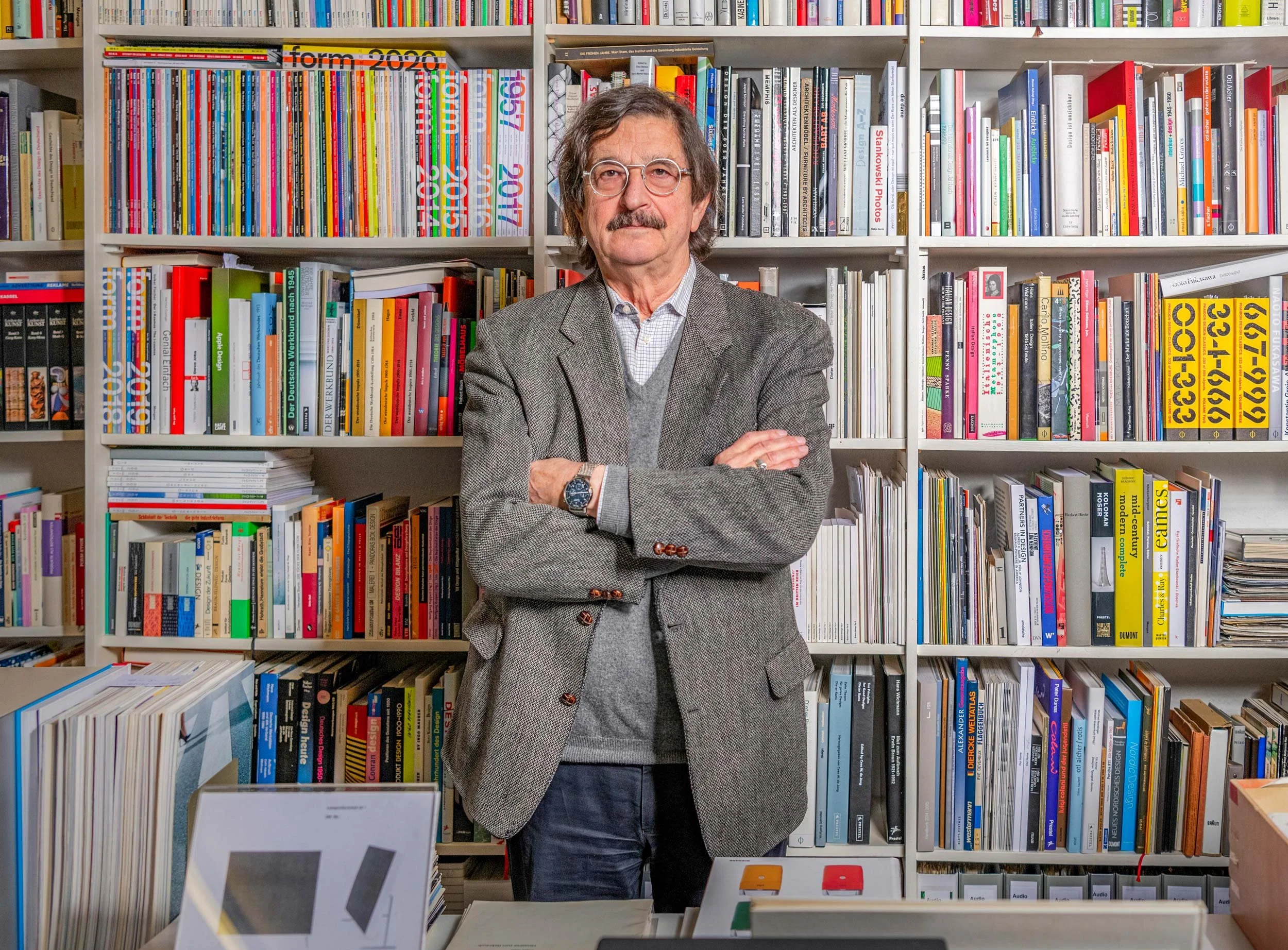 Environmental portrait of Werner Ettel standing in front of shelves filled with design books at the Braun-Sammlung Ettel.