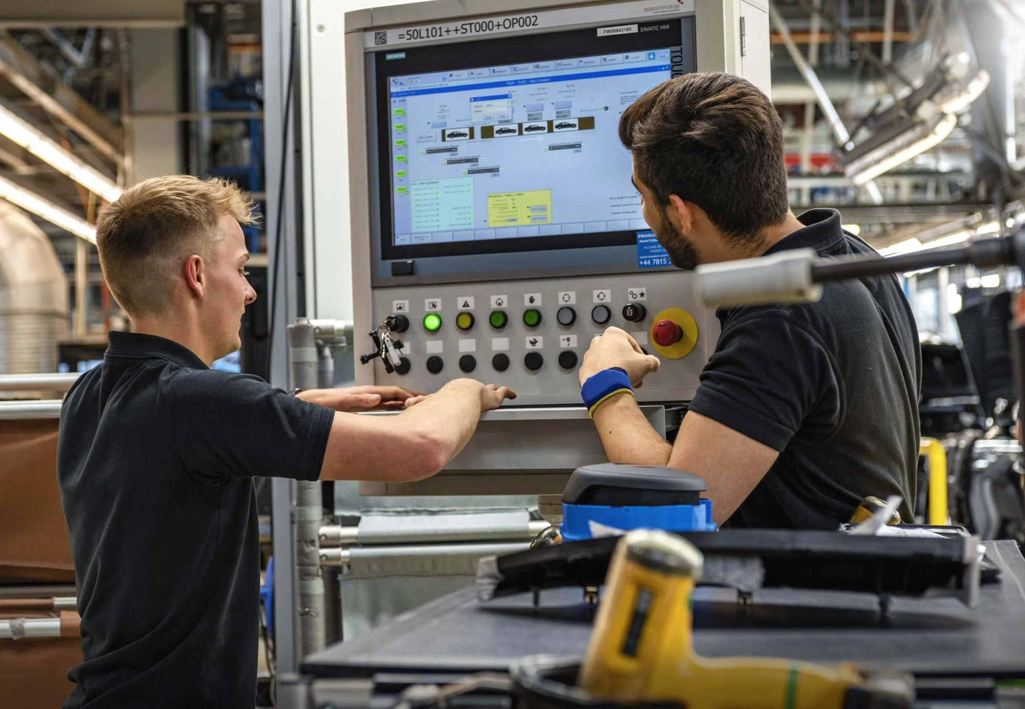 Two operators monitoring industrial control panel on active production line – industrial automation photography London