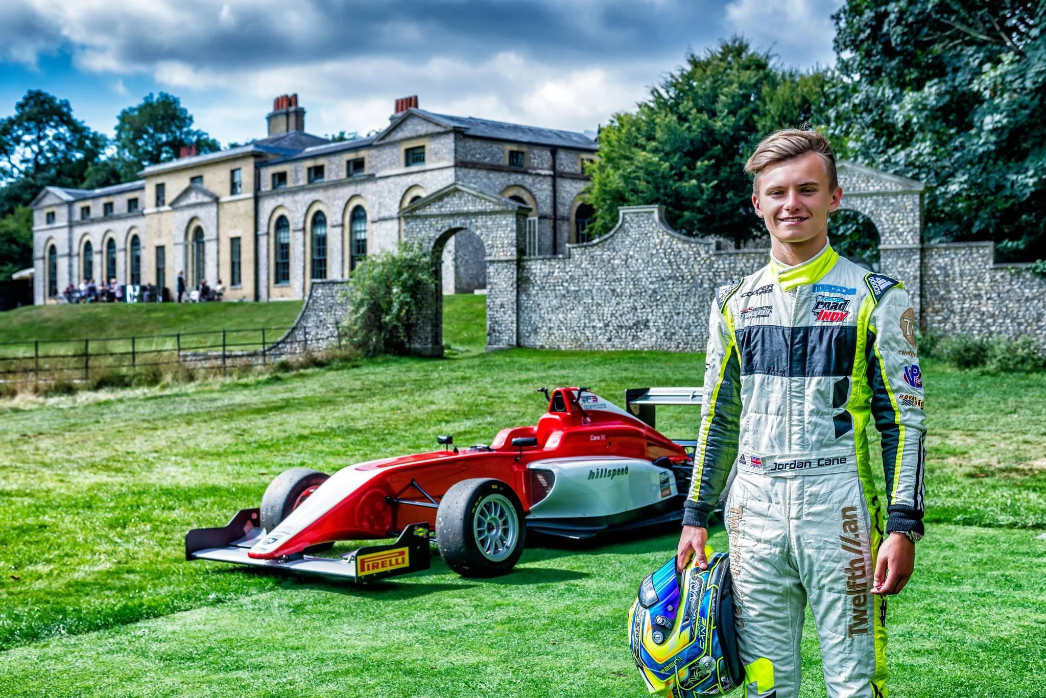 Young racing driver holding helmet in front of red formula car at outdoor motorsport event – automotive events photography London