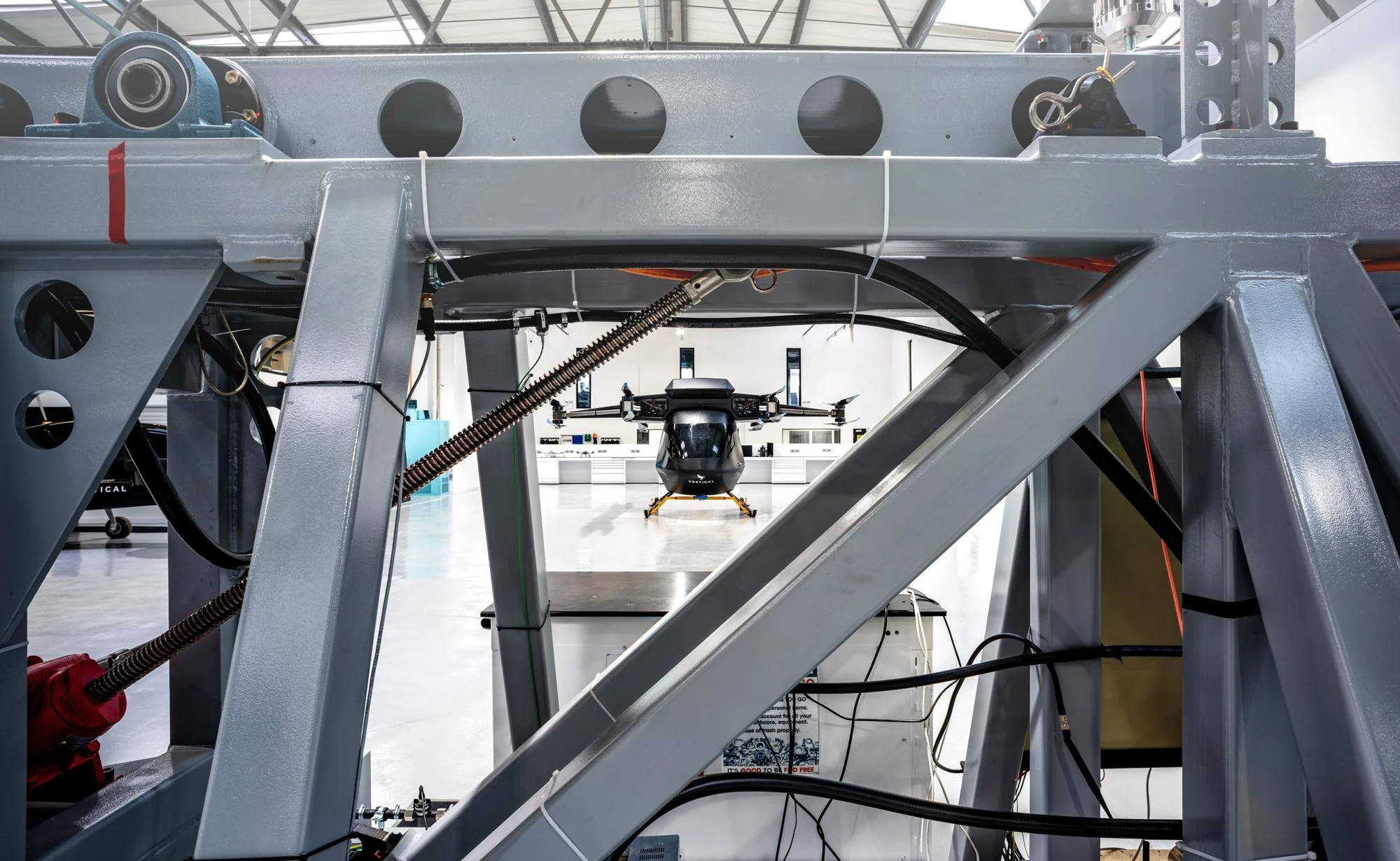 VX4 eVTOL prototype viewed through metal rigging inside an aerospace hangar during early development – aerospace manufacturing photography London