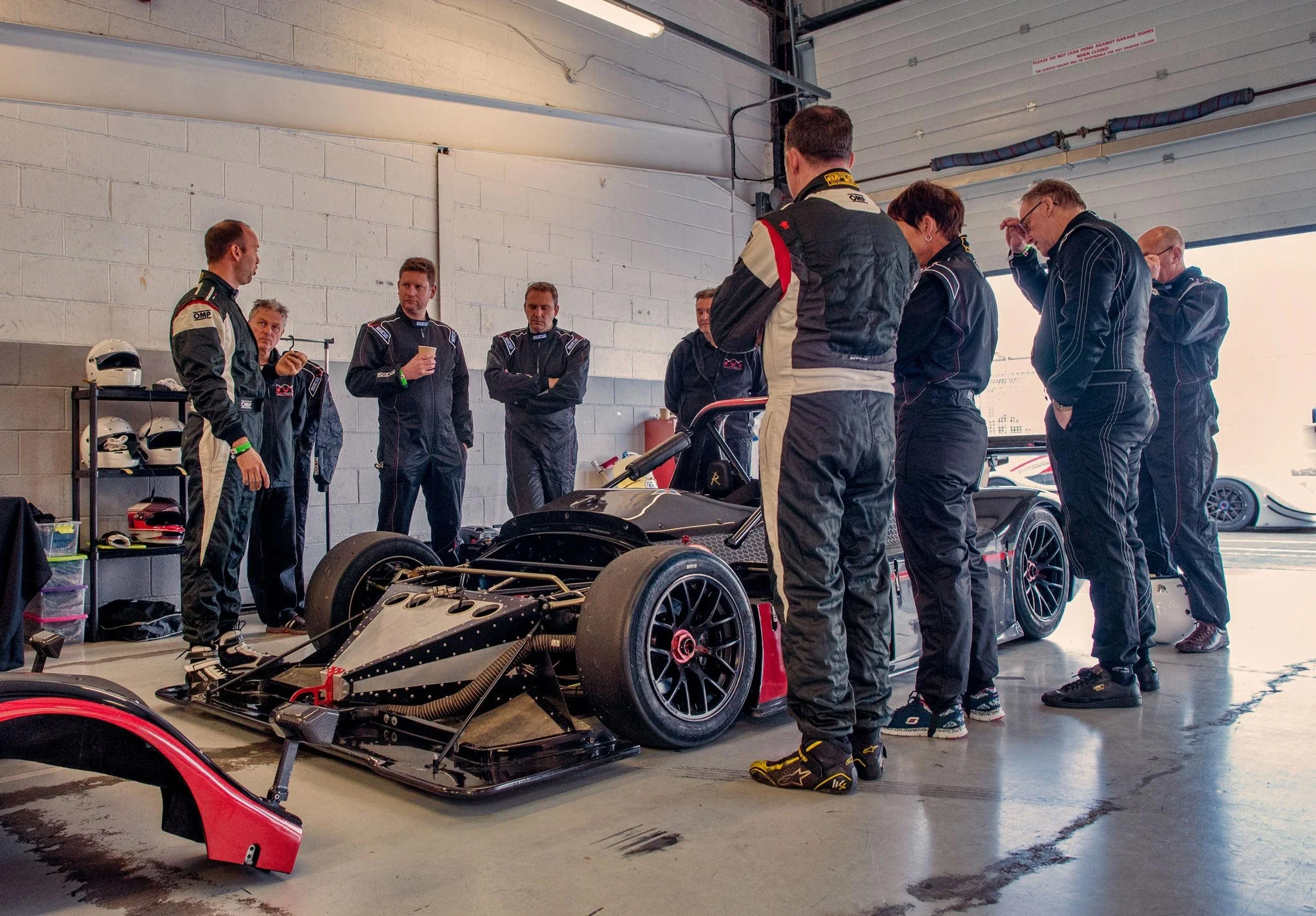 Corporate team briefing in the paddock garage at Silverstone track day with formula racing car – automotive events photography London