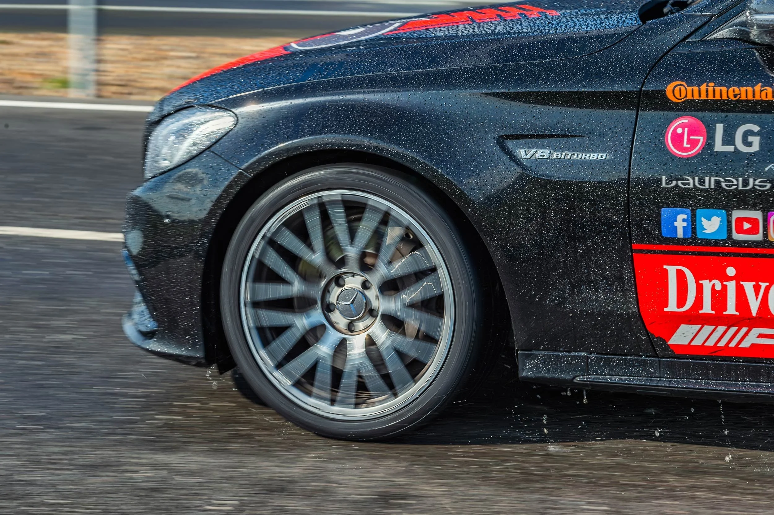 Mercedes-AMG V8 Biturbo badge and spinning wheel on a wet Mercedes-Benz World experience car