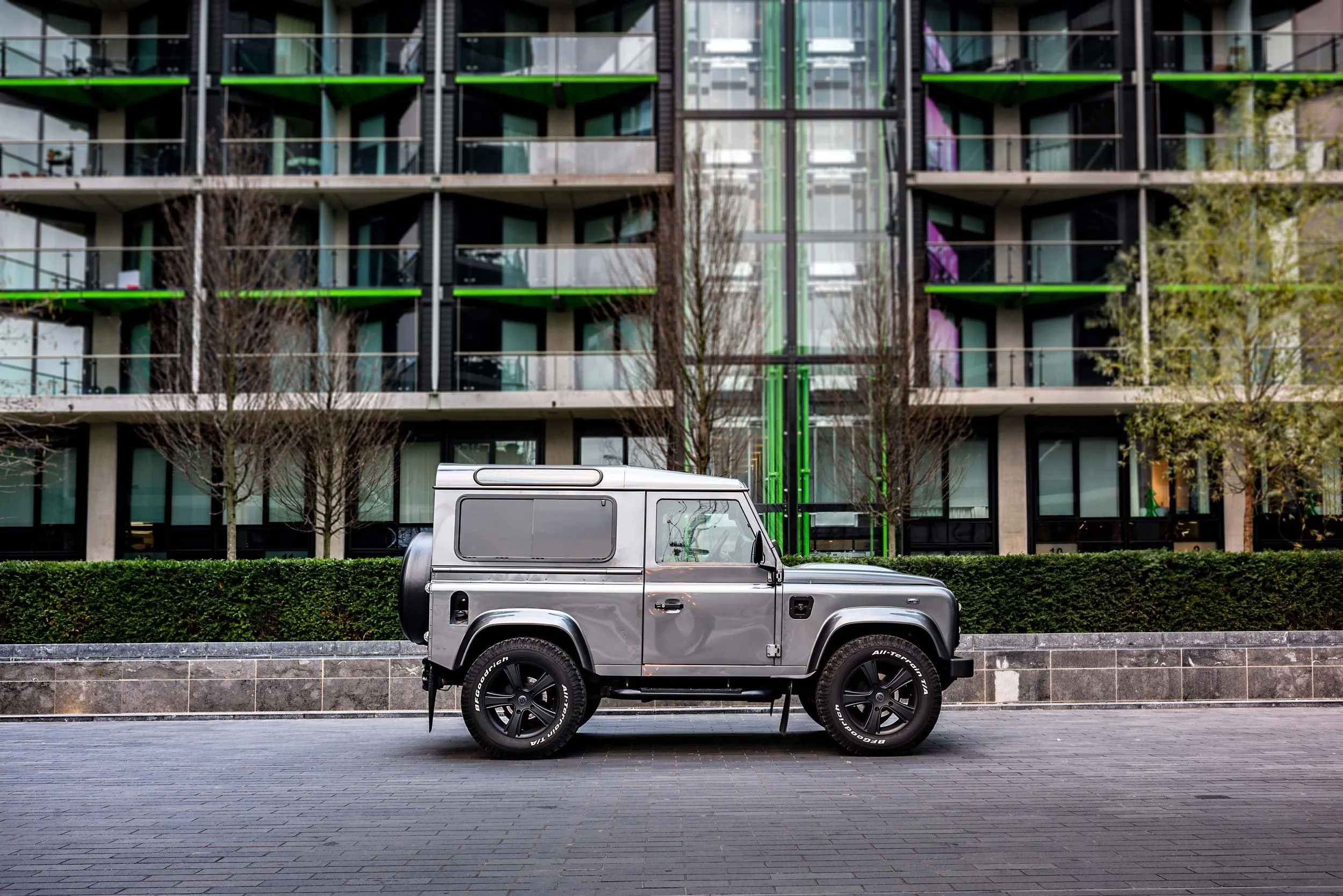 Side profile of a customised grey Land Rover Defender 90 parked outside a contemporary London apartment building.