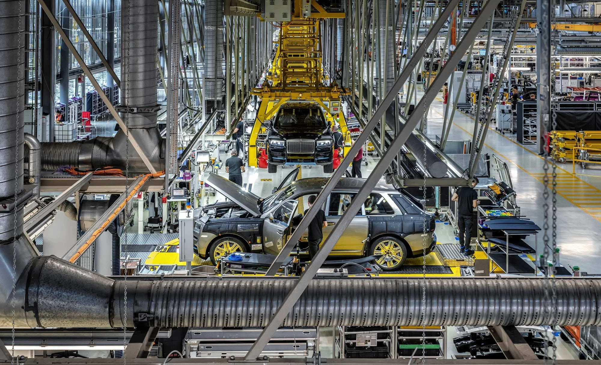 Elevated view of busy automotive assembly line with vehicles, engineers and tool stations in a large manufacturing plant – industrial photographer London