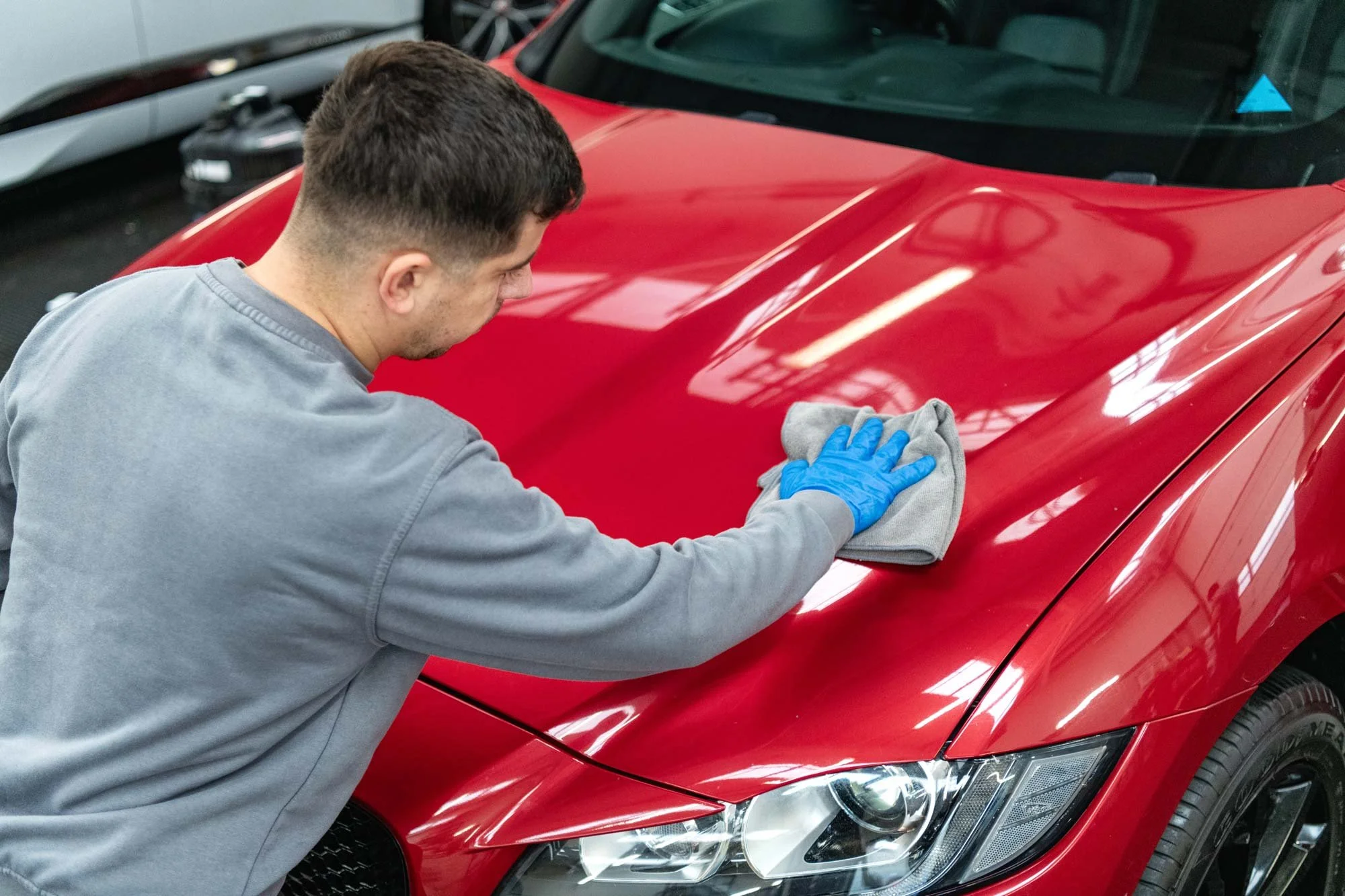 Technician carefully polishing the bonnet of a red car in a professional detailing bay – car detailing photography