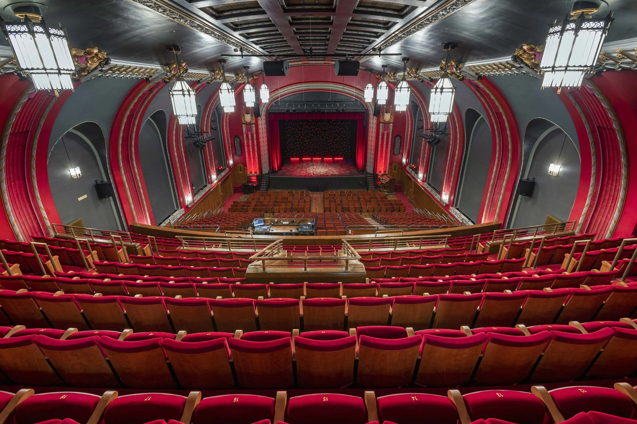 Broadway Theatre auditorium viewed from the dress circle, with red seating, decorative arches, suspended lighting and the stage.