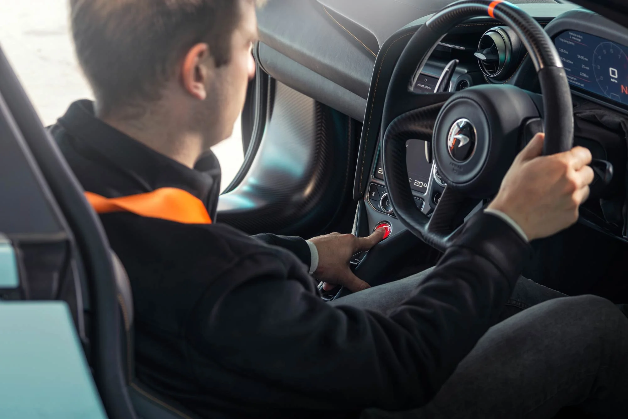 Engineer pressing glowing ignition button inside sports car cockpit during high-performance testing – industrial test facility photography London