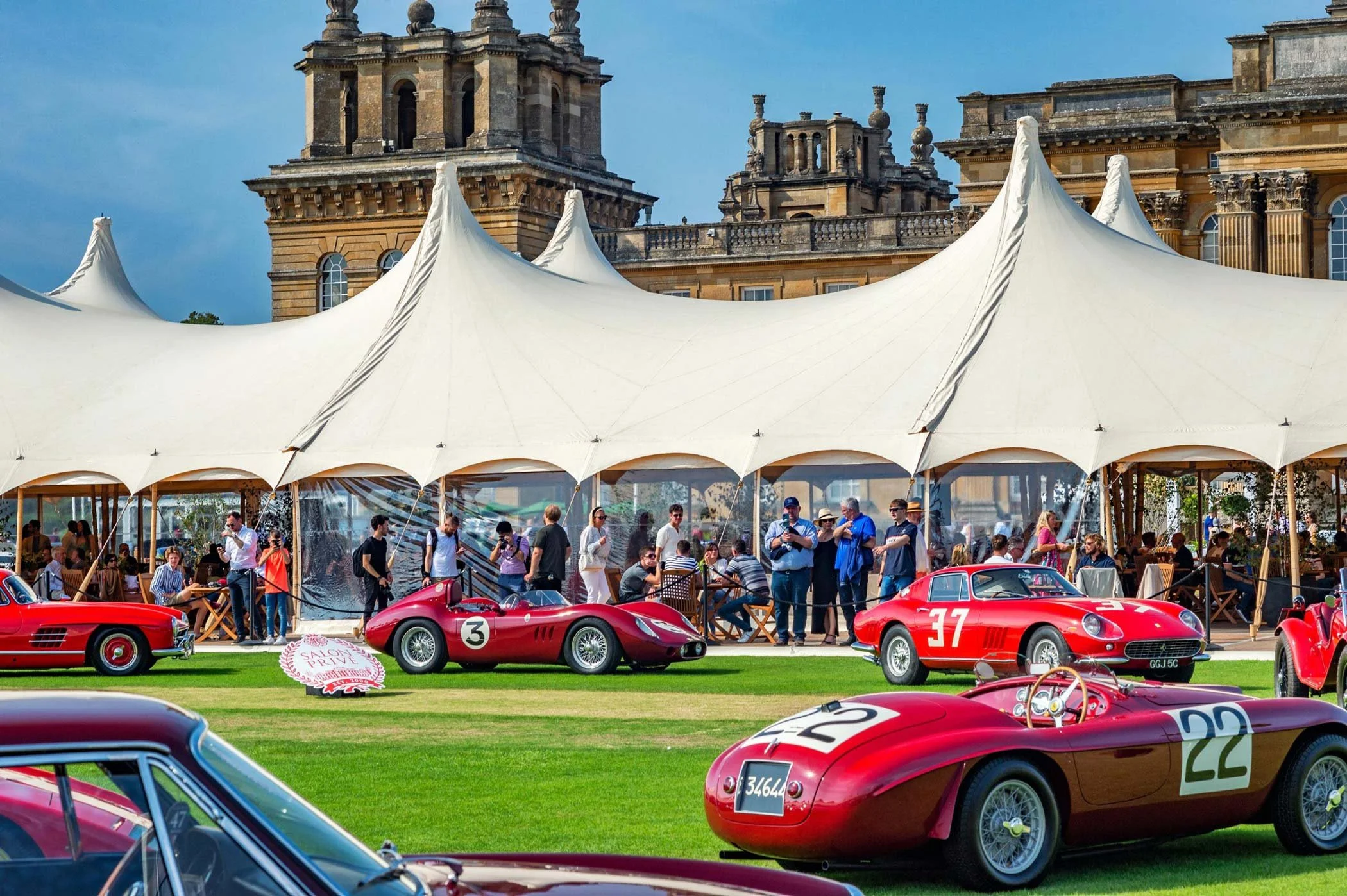 Classic red Ferrari racing cars on display at a prestigious historic automotive event with large tents and grand architecture – classic car events photography London