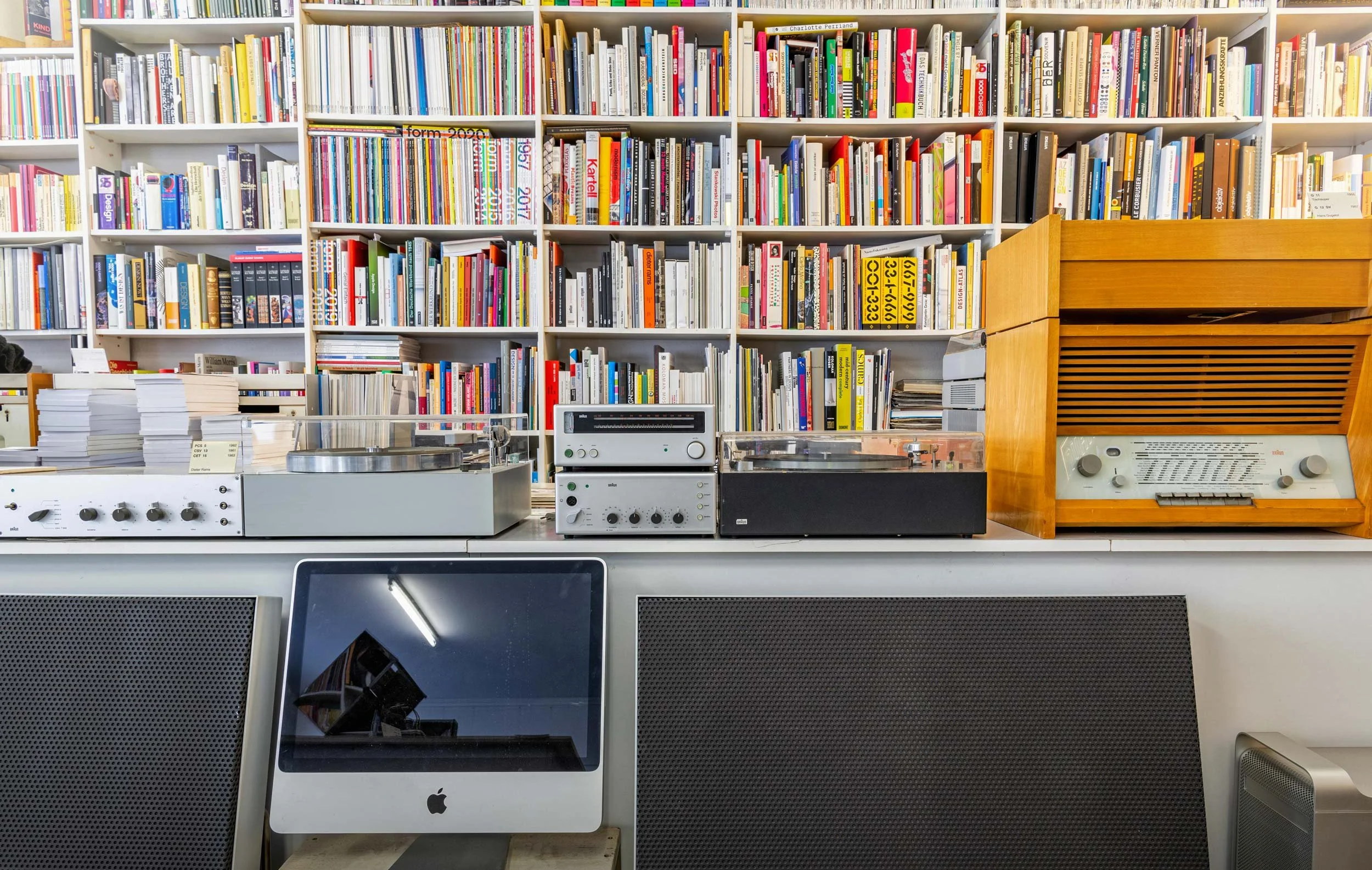 Historic Braun turntables, radio receivers and amplifiers displayed in front of shelves of design books.
