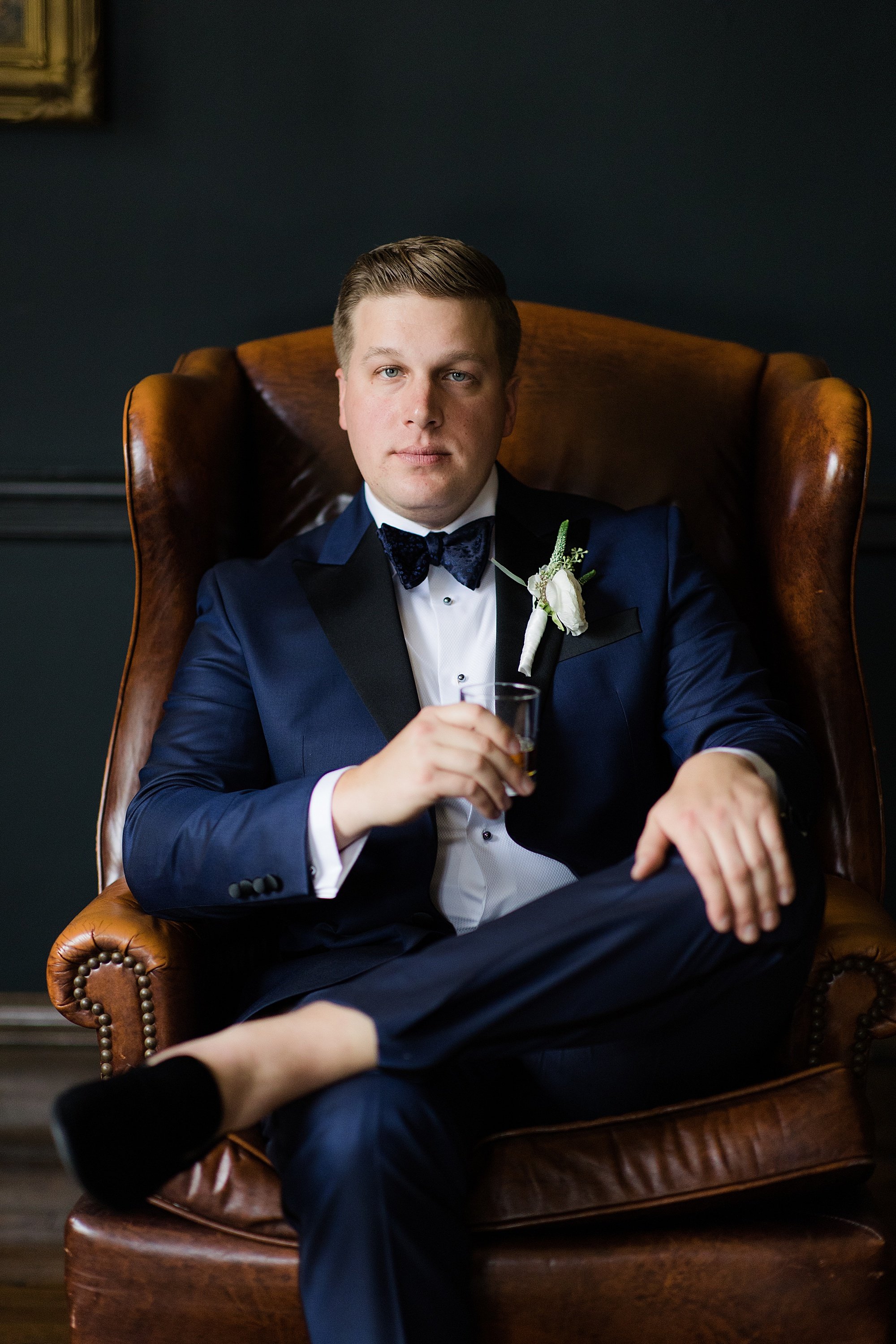 Groom sits in chair with whiskey 