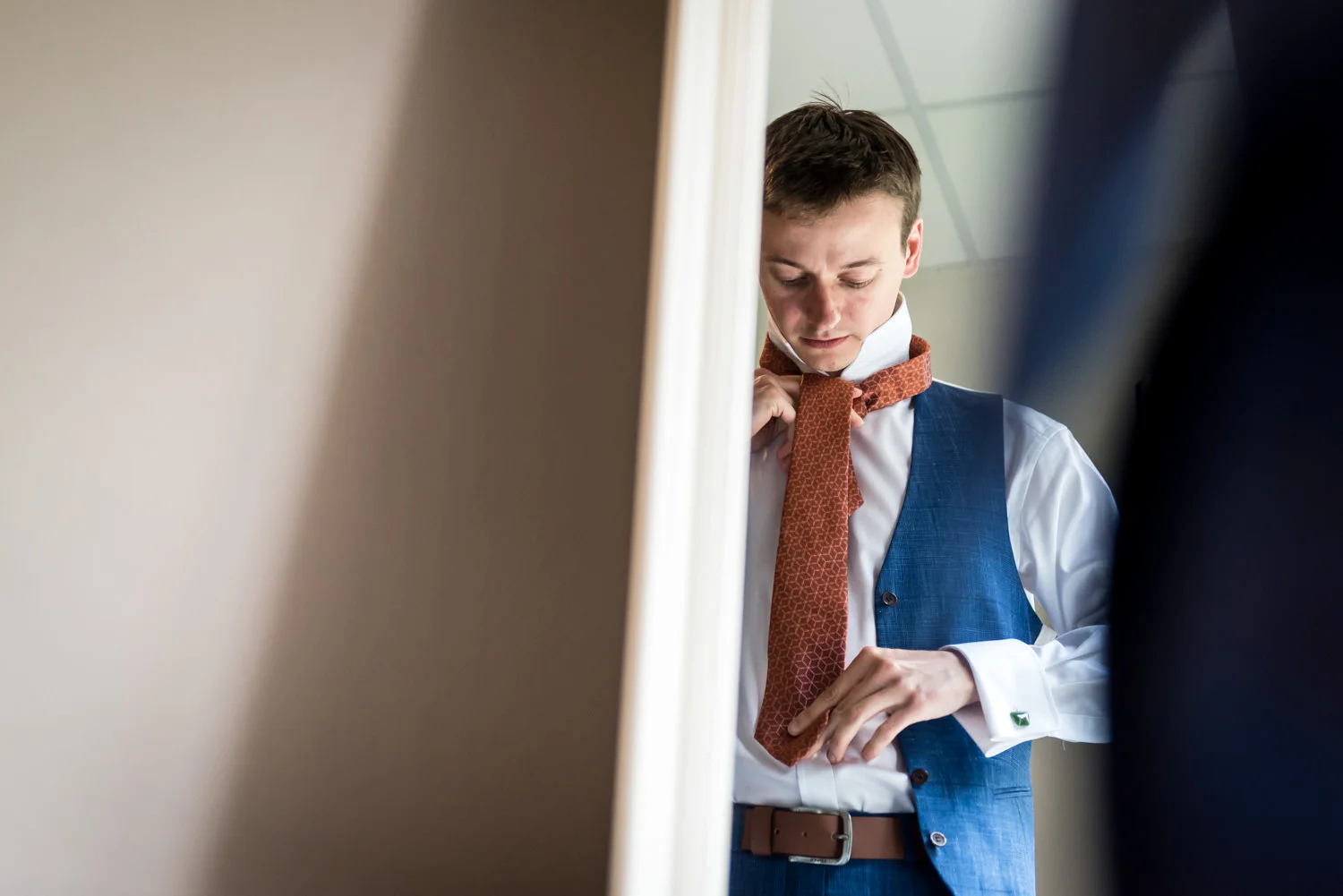 groom is looking tot his tie in the mirror