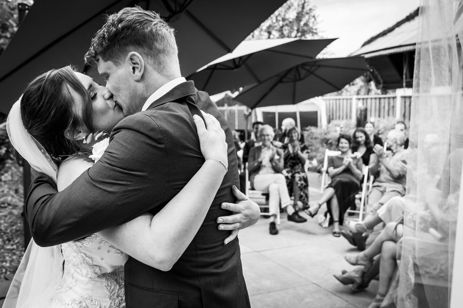 De kus het mooiste moment van de trouwdag, een goede trouwfotograaf legt dit vast, mooi is ook dat de gasten op de achtergrond te zien zijn.