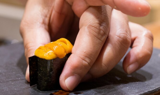 Chef placing a piece of uni gunkan sushi on plate