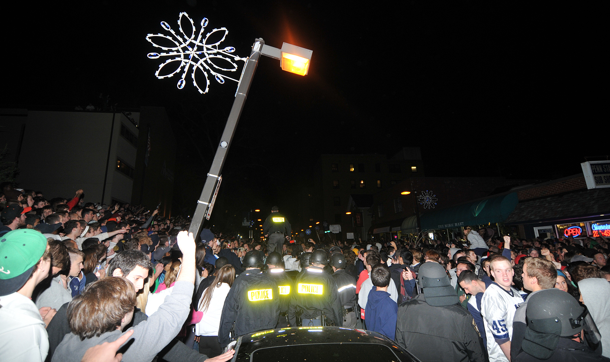  A policeman (center) walks on top of a car to use pepper spray on a rioter on Beaver Avenue during the riots on Wednesday night. The lightpole was also being torn down by rioters. 