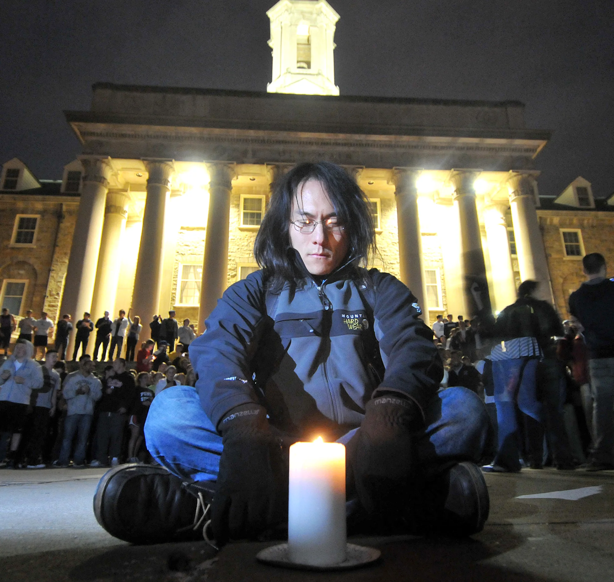 Brenton Mitchell, 28, of State College, sits on the ground with a candle at Old Main during the beginning of the riot in State College on Wednesday night. The crowd gathered here and then moved downtown. Mitchell got stepped on multiple times.