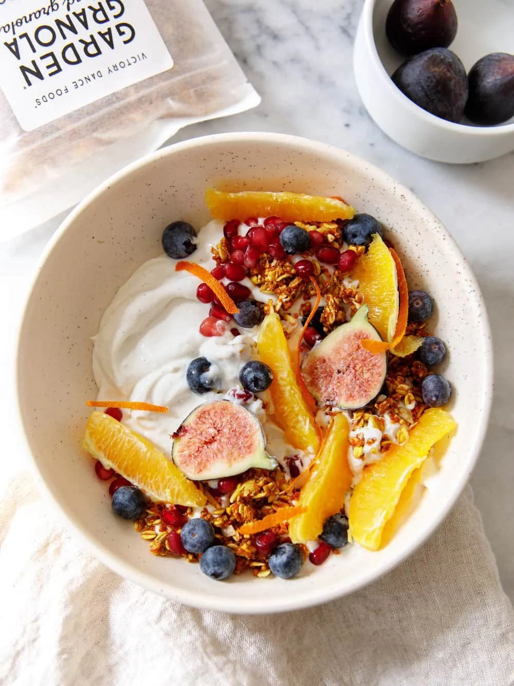 Orange and pomegranate yogurt bowl with Carrot Turmeric Garden Granola® on top, photographed from overhead in a neutral bowl.