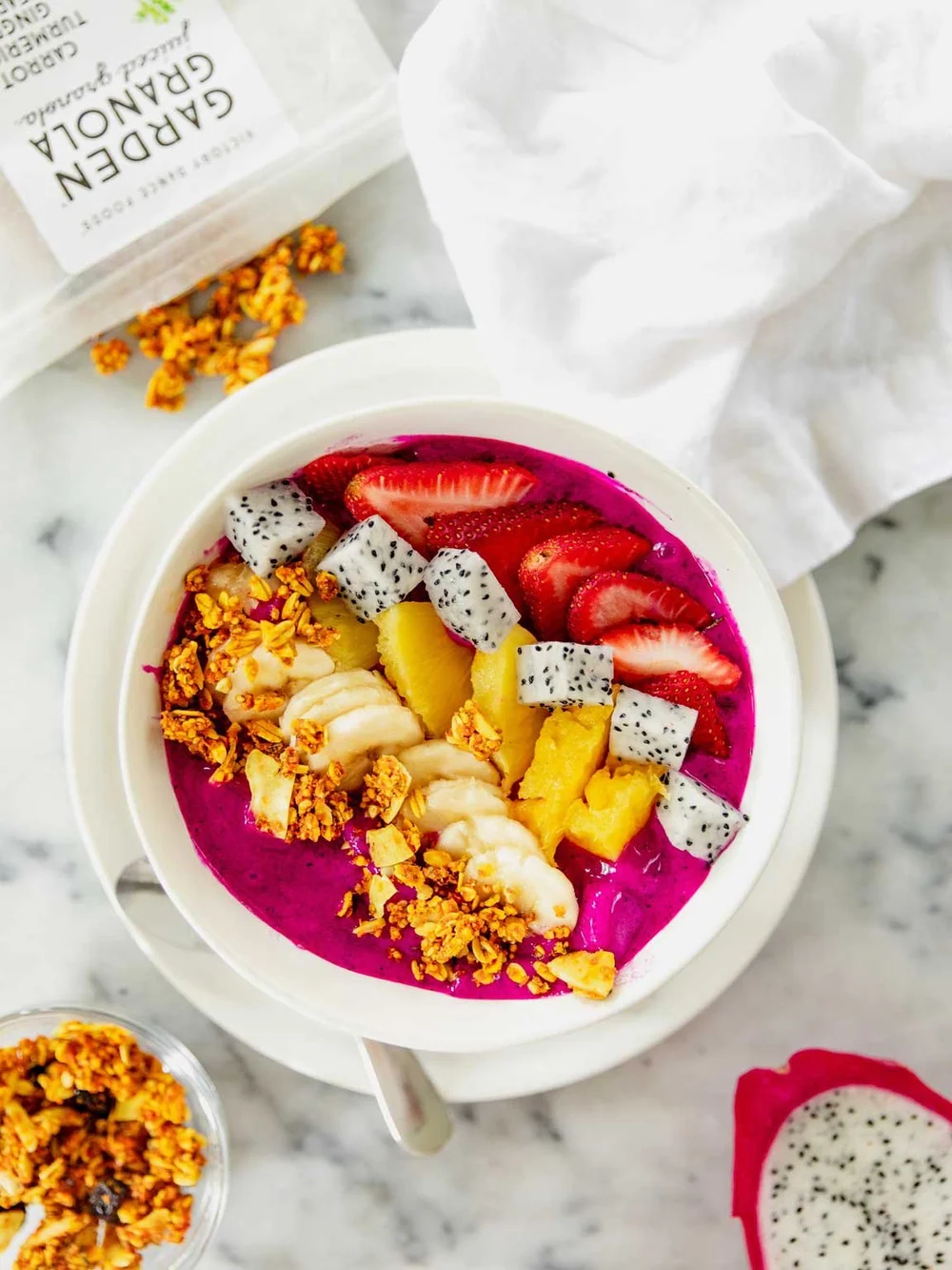 A vibrant magenta dragon fruit smoothie bowl topped with carrot turmeric garden granola and fresh fruit.