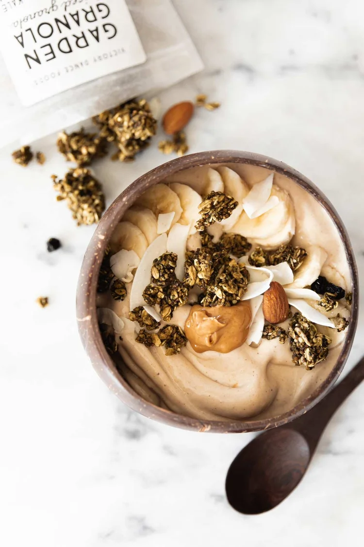 A vibrant green smoothie bowl made with banana and peanut butter, topped with kale matcha granola and fresh fruit.