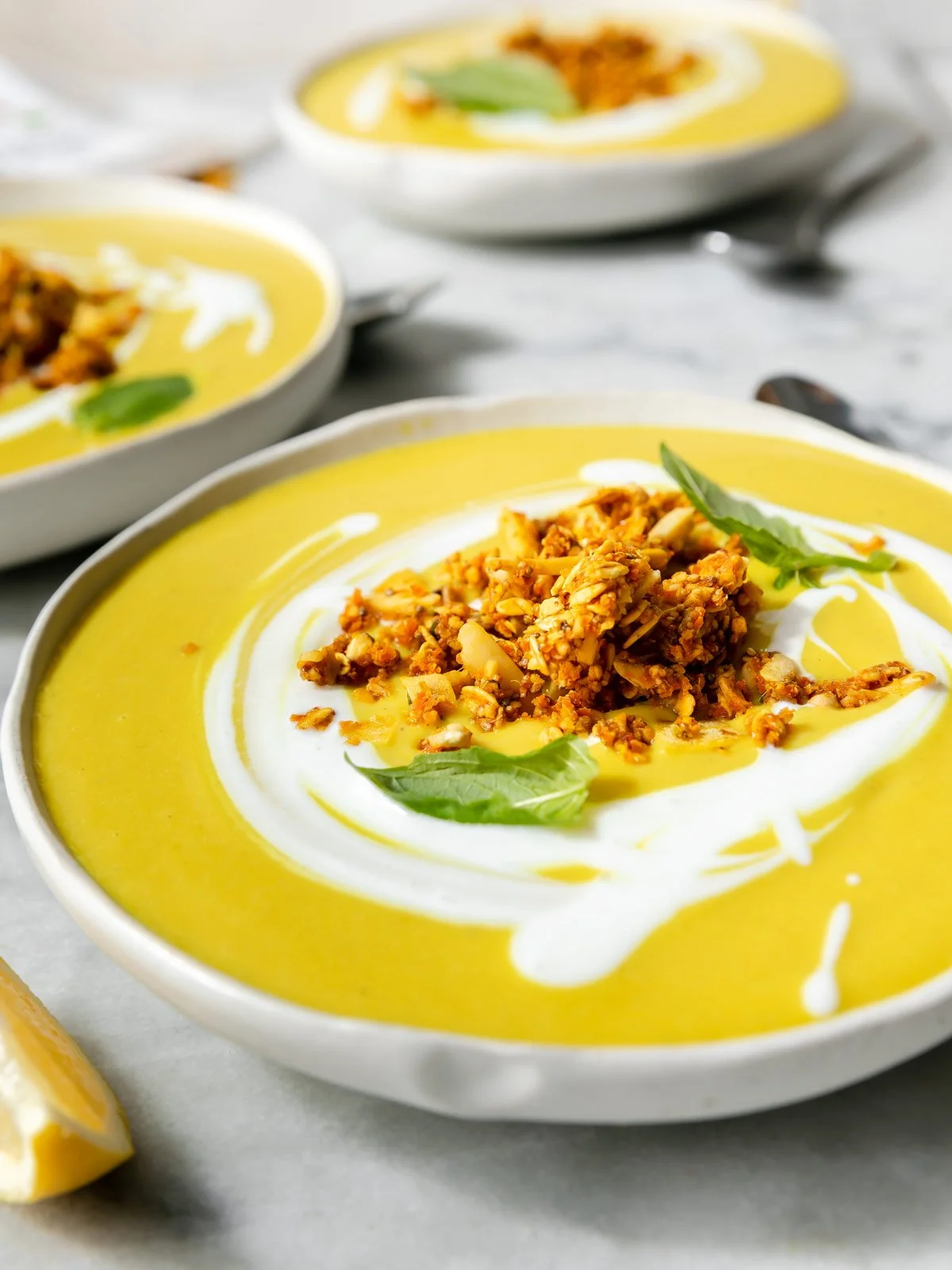 Close-up of creamy golden turmeric soup in white bowl topped with crunchy Garden Granola Carrot Turmeric and fresh basil
