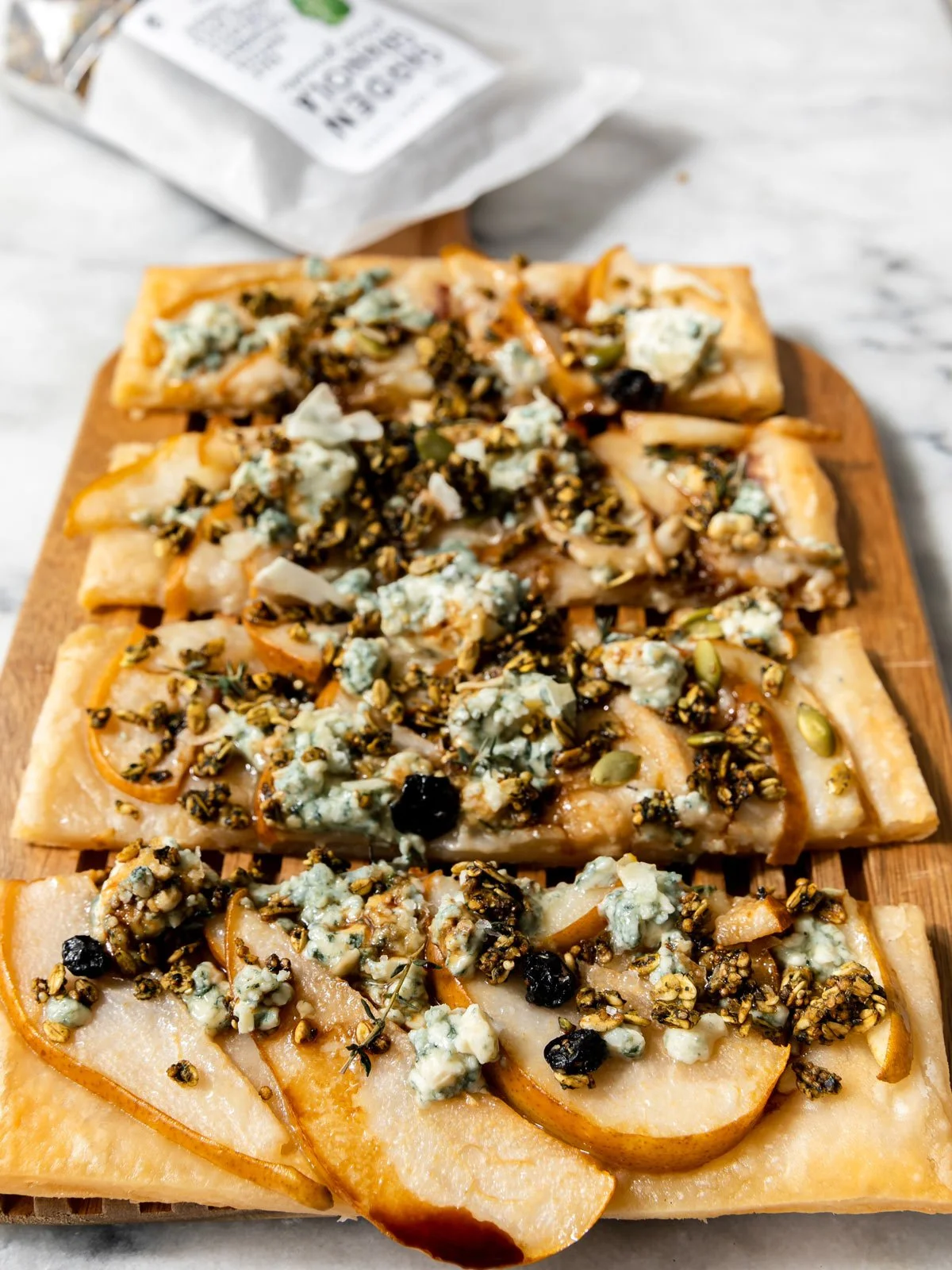 Close-up of sliced gluten-free pear flatbread showing golden puff pastry topped with caramelized pear slices, Gorgonzola cheese, and crunchy granola