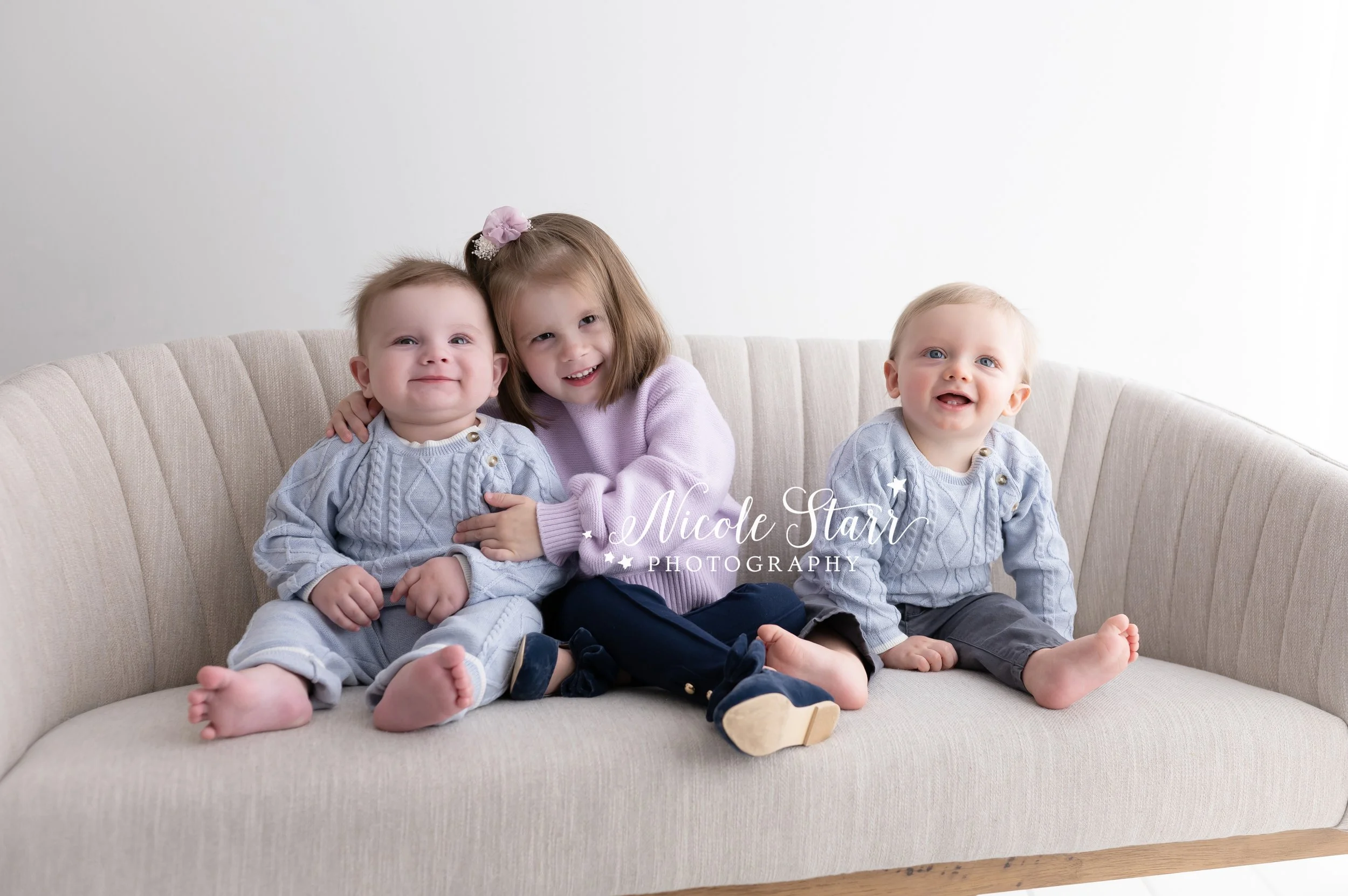 three cousins sit together on tan couch in studio during family portraits with NY family photographer Nicole Starr Photography