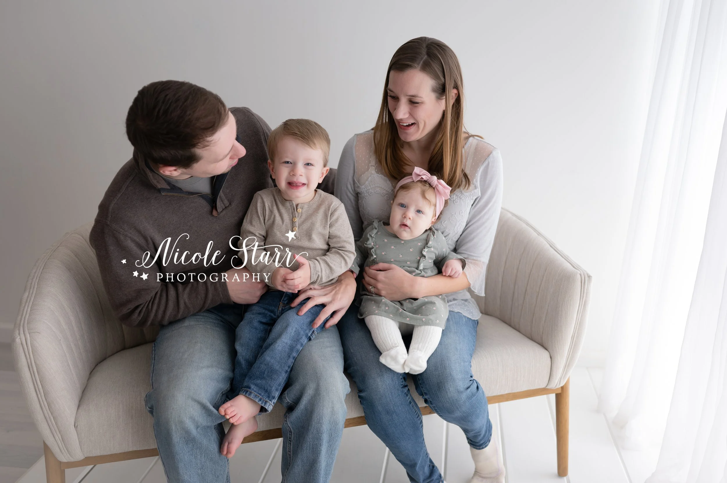 family of four laughs together on tan couch in studio with NY family photographer Nicole Starr Photography