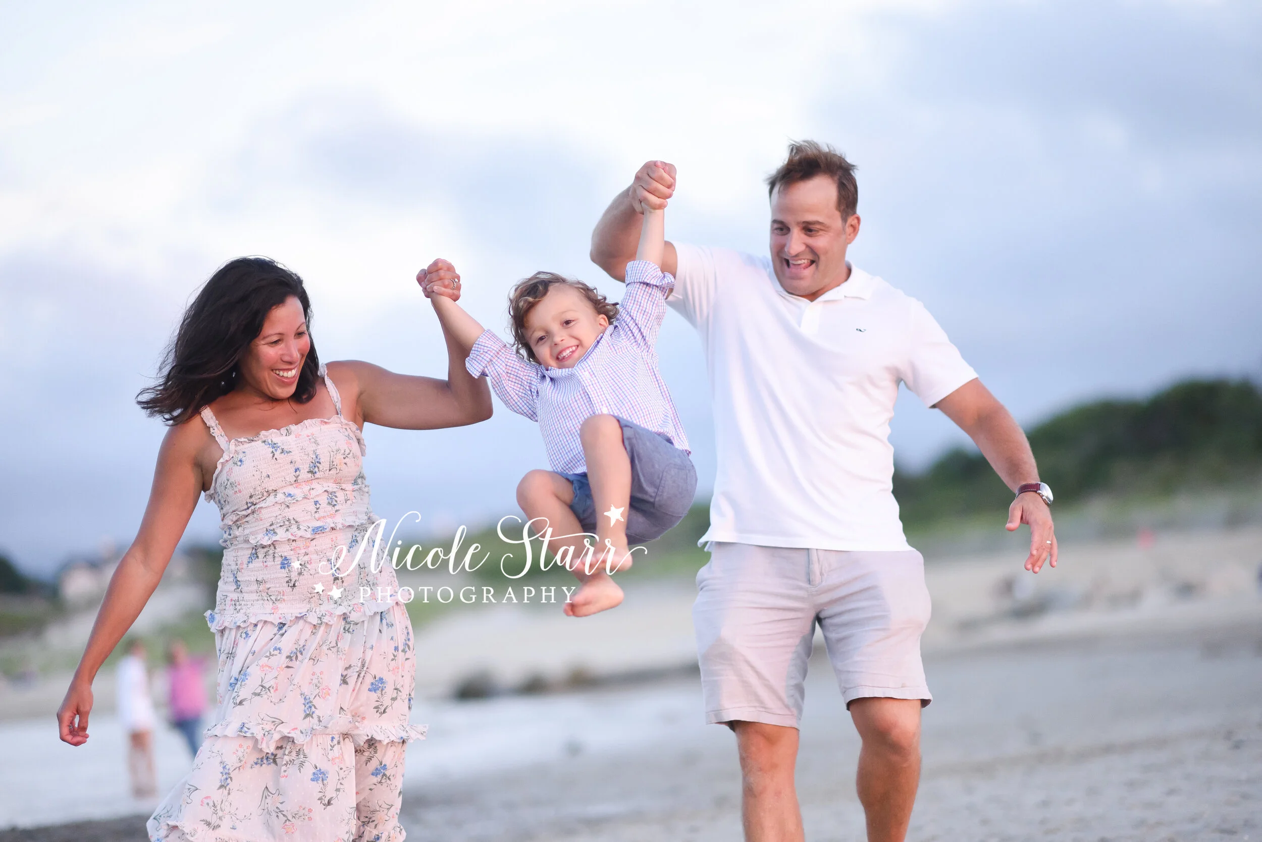 family lifts son walking along beach in front of ocean photographed by Cape Cod family photographer Nicole Starr Photography