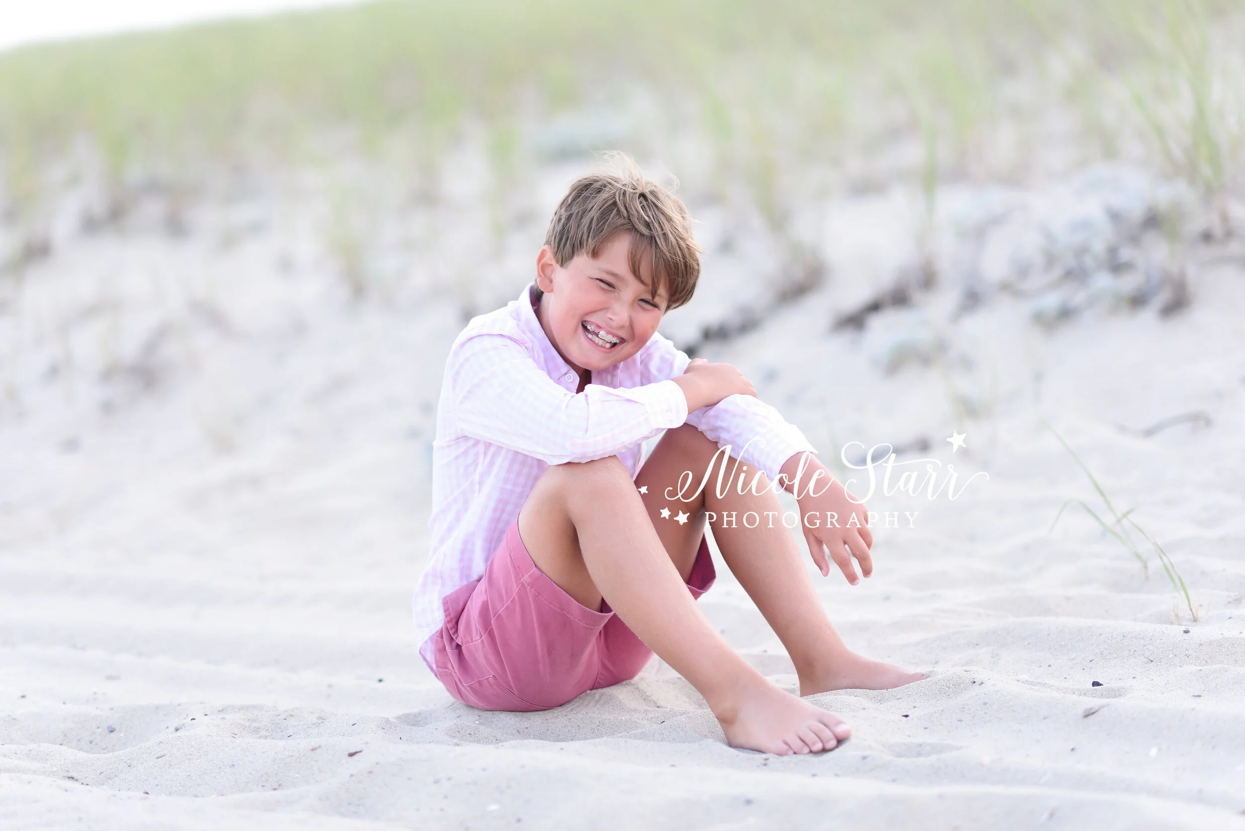 little boy in gingham shirt sits on the beach photographed by Cape Cod family photographer Nicole STarr Photography