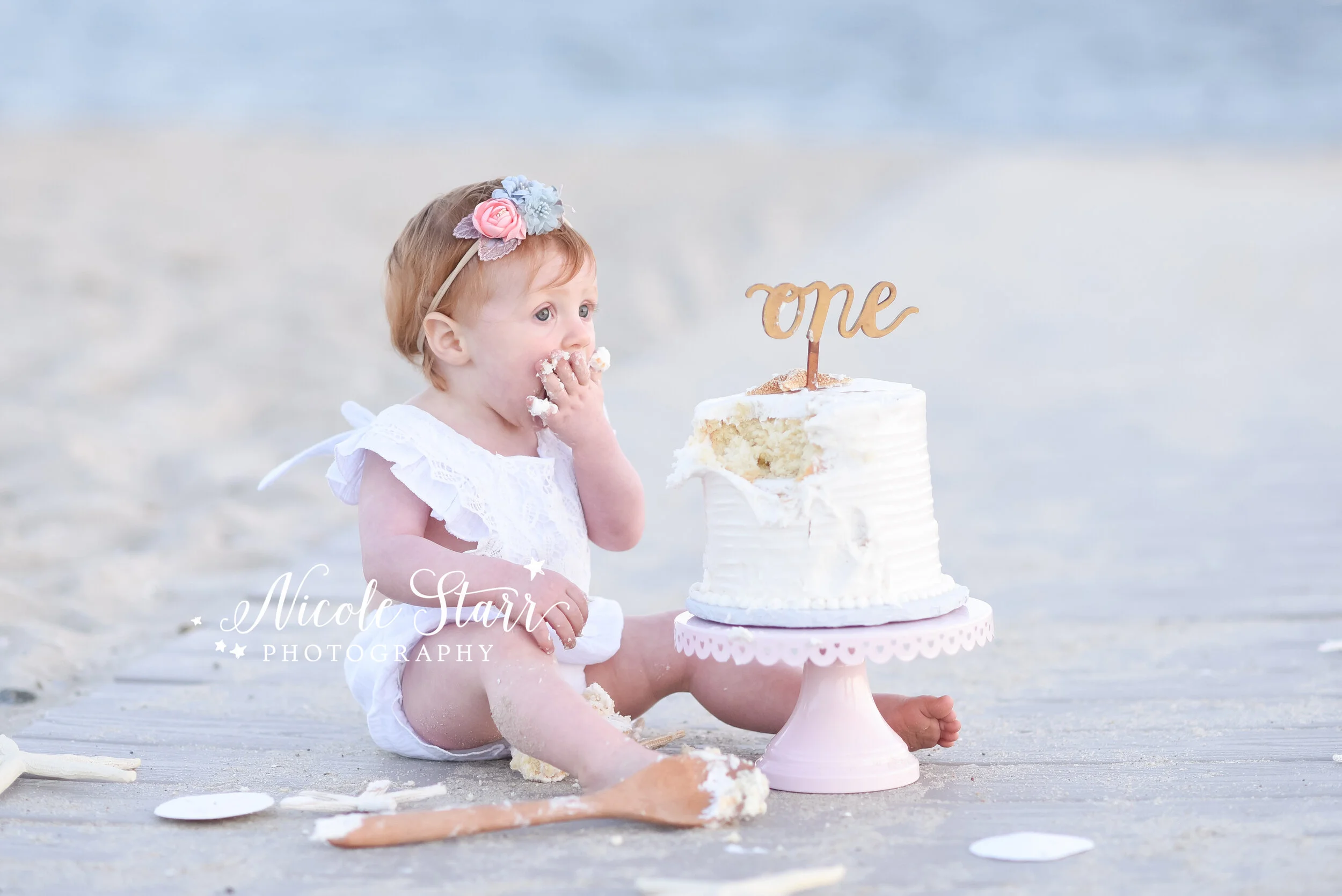 baby girl looks at elegant white cake for cake smash with Cape Cod family and cake smash photographer Nicole Starr Photography&nbsp;