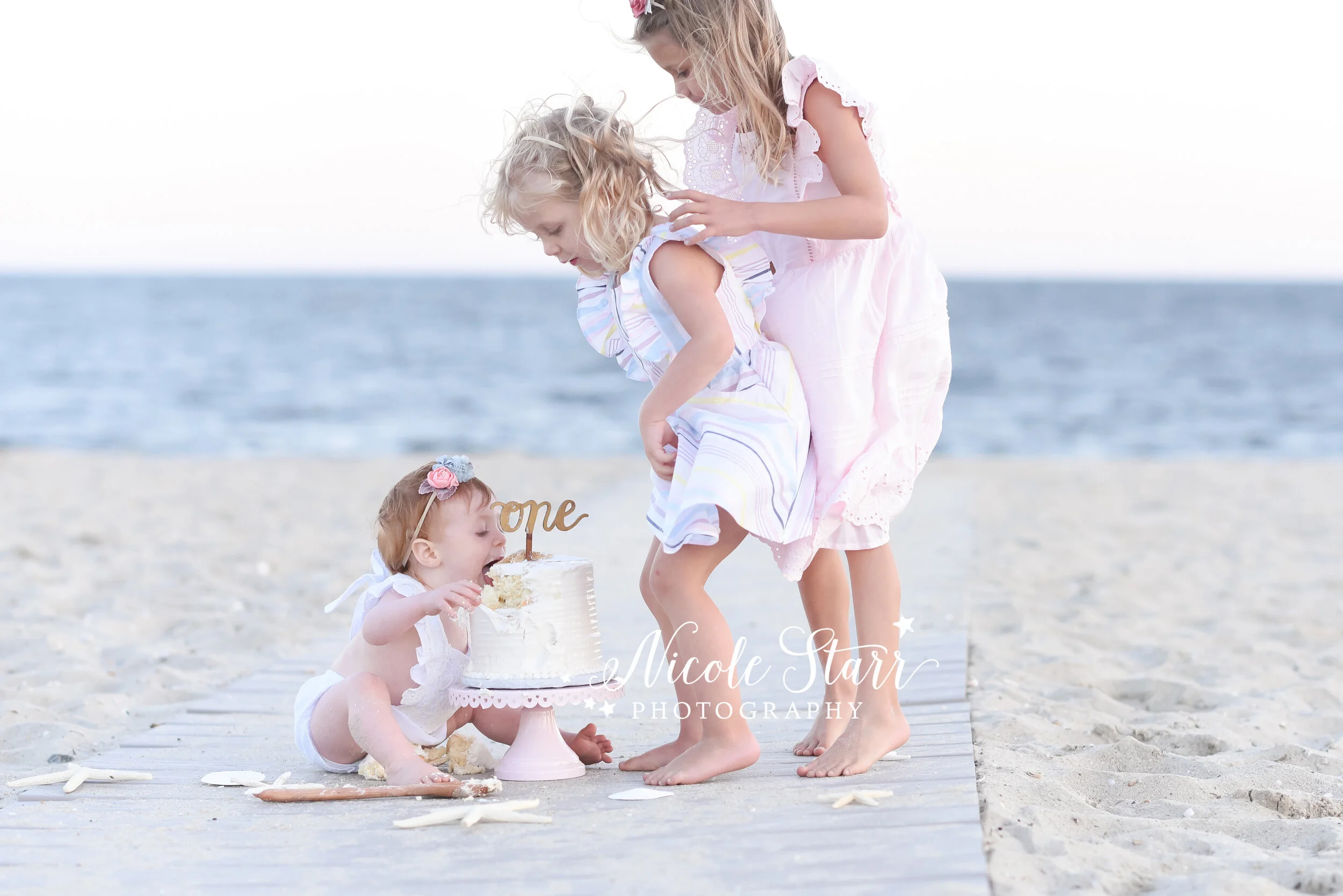 big sisters help birthday girl with cake smash photographed by Cape Cod family and cake smash photographer Nicole Starr Photography&nbsp;