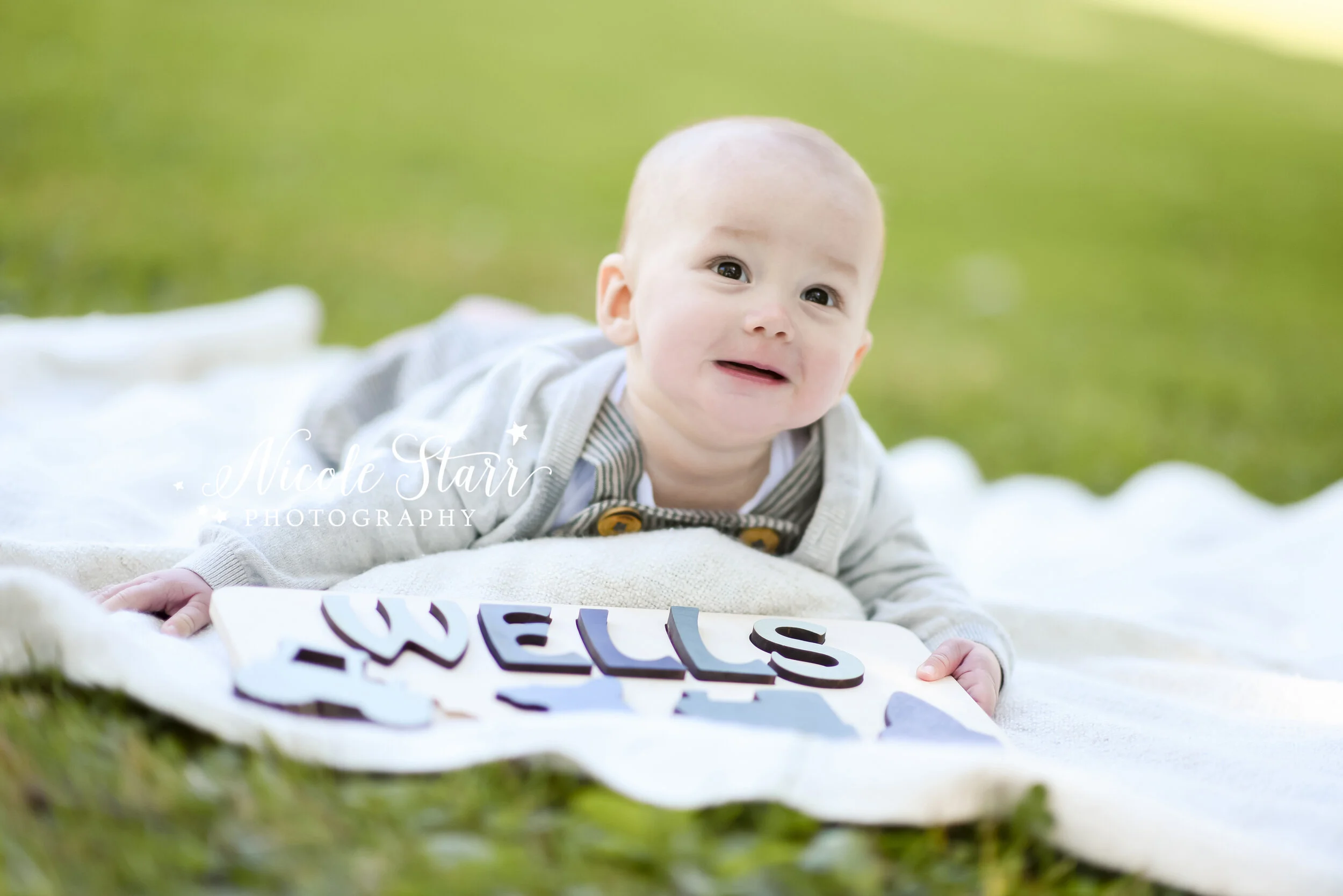 baby poses with wooden sign during milestone portraits in Congress Park photographed by Saratoga Springs and Delmar NY family photographer Nicole Starr Photography