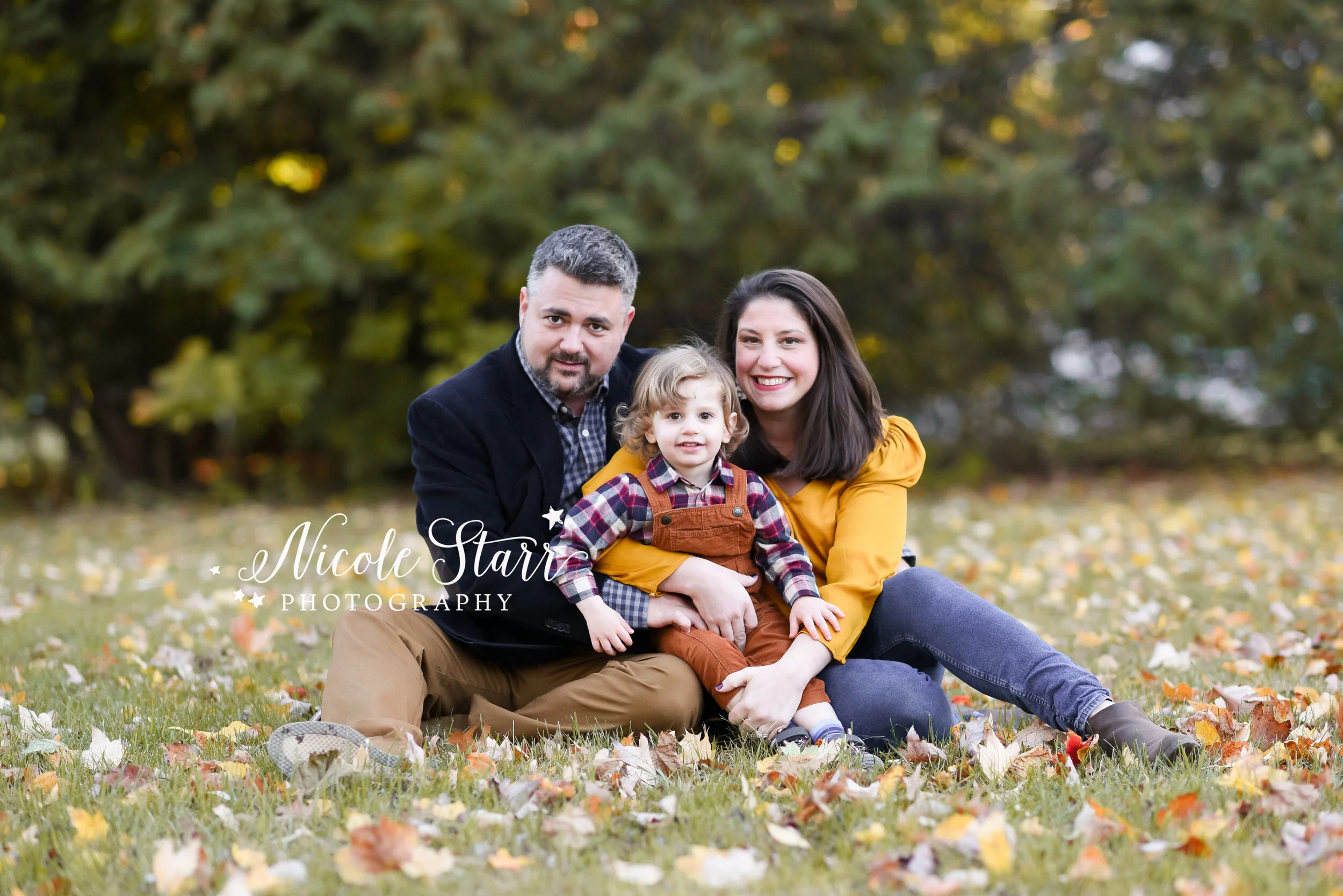 family of three plays in leaves during family photos with Albany NY family photographer Nicole Starr Photography