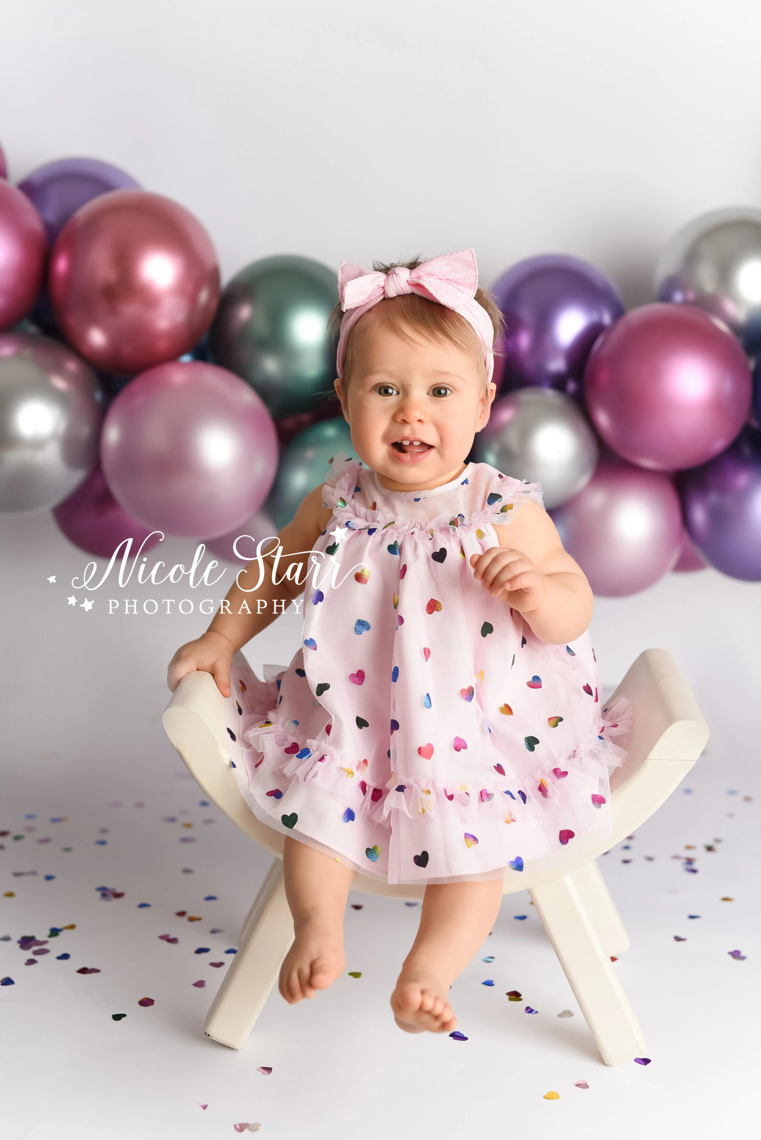 toddler in heart dress poses in front of metallic balloon garland photographed by Delmar NY cake smash photographer Nicole Starr Photography