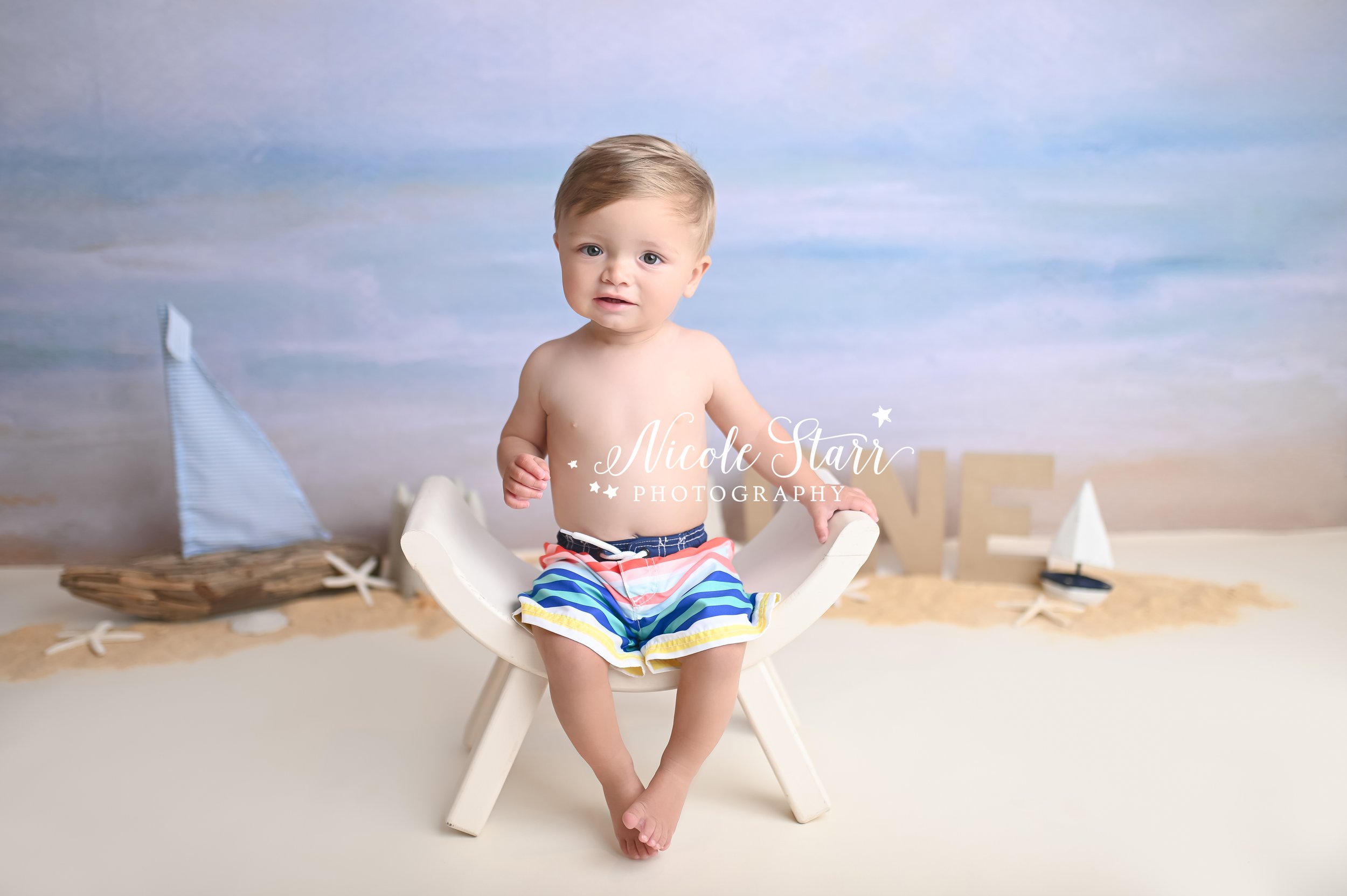 baby sits on white bench during beach cake smash in Saratoga Springs