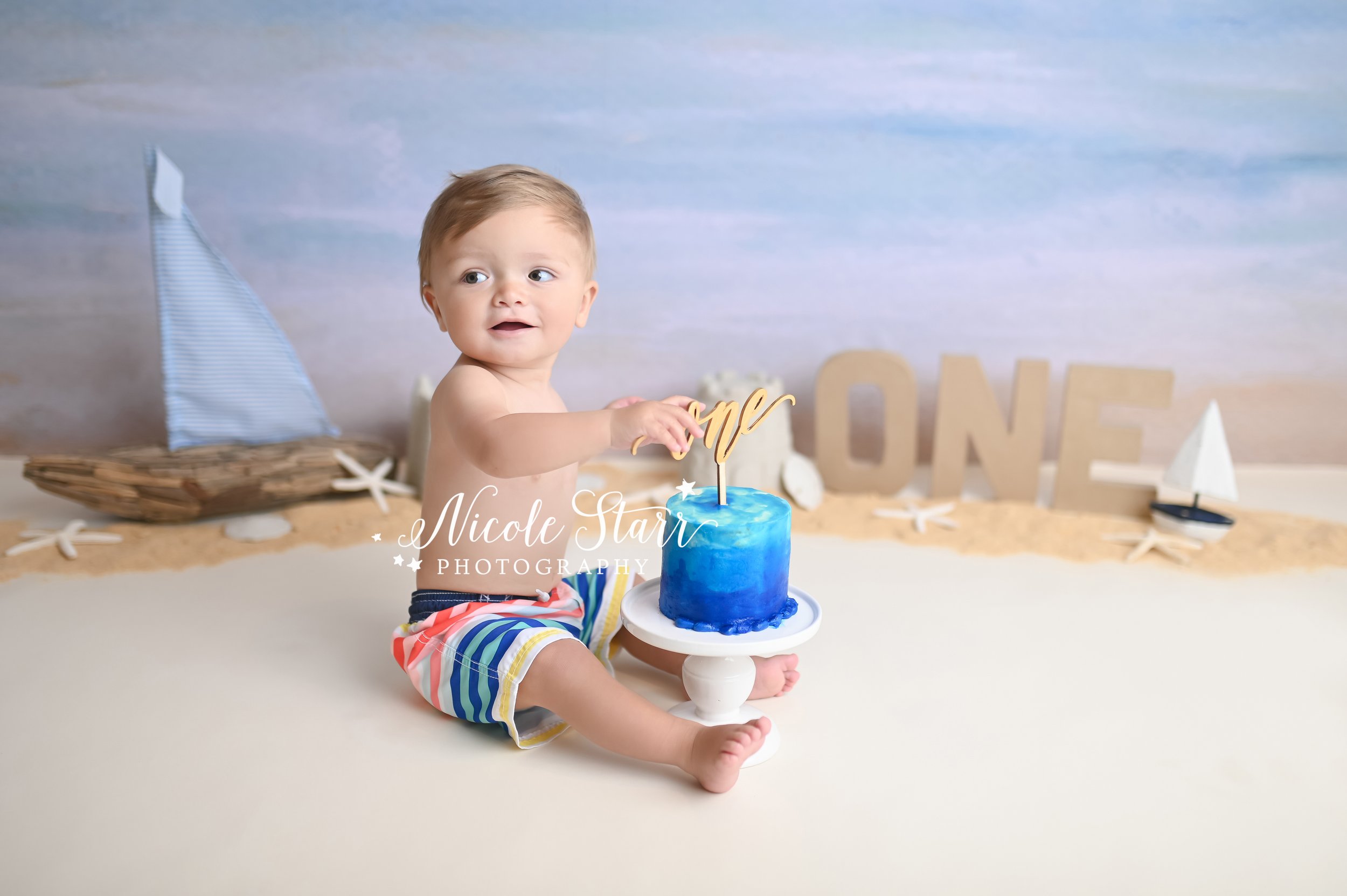 baby plays with blue cake during beach cake smash with Saratoga Springs NY cake smash photographer Nicole Starr Photography 