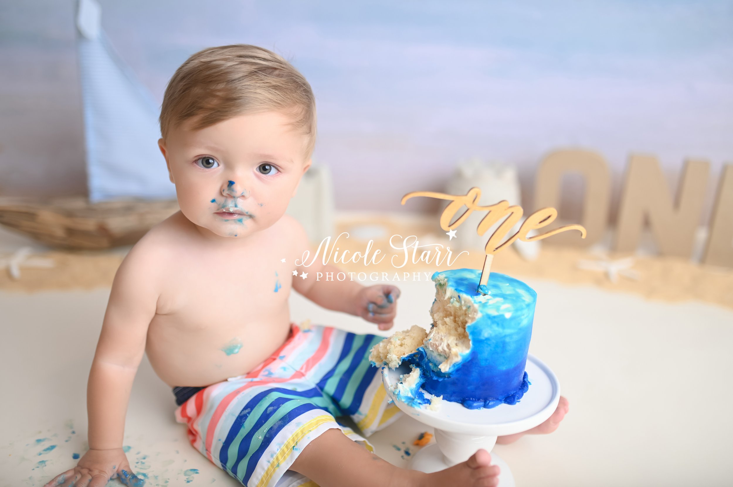 toddler frowns with blue icing on his nose during cake smash with Saratoga Springs NY cake smash photographer Nicole Starr Photography 