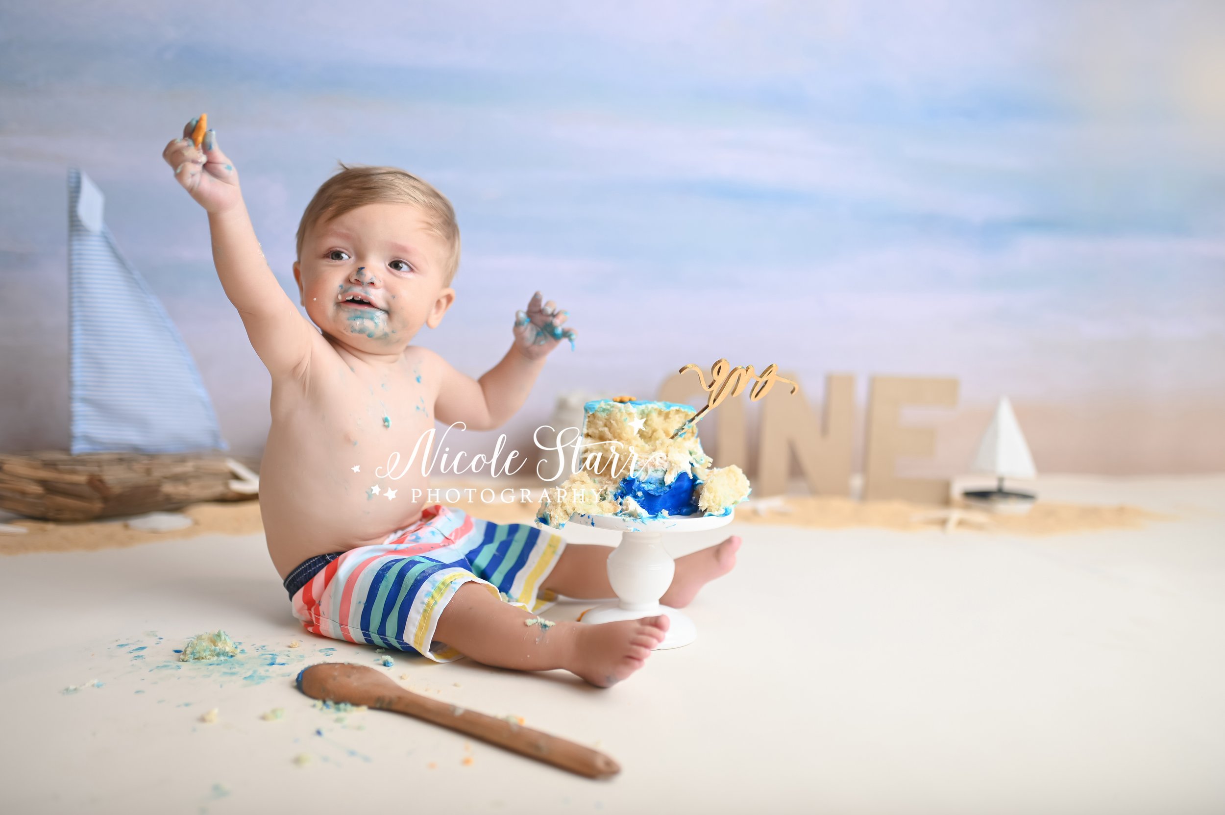 baby cheers showing off blue hands during cake smash with Saratoga Springs NY cake smash photographer Nicole Starr Photography 