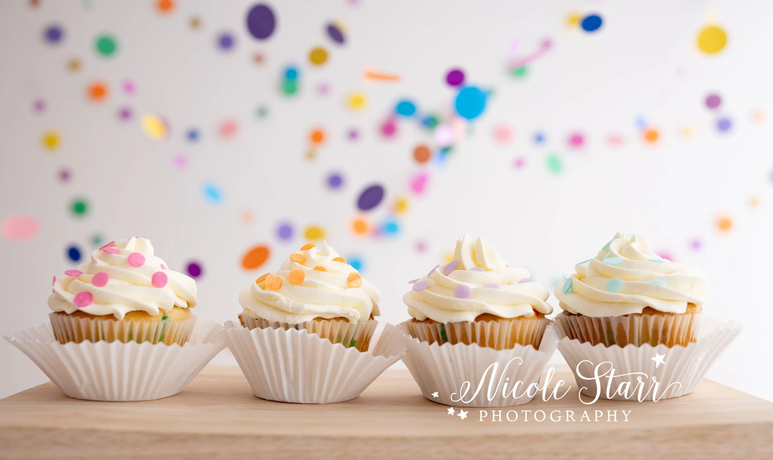 four confetti cupcakes for cake smash with friends in front of rainbow streamers in Saratoga Springs studio with Nicole Starr Photography