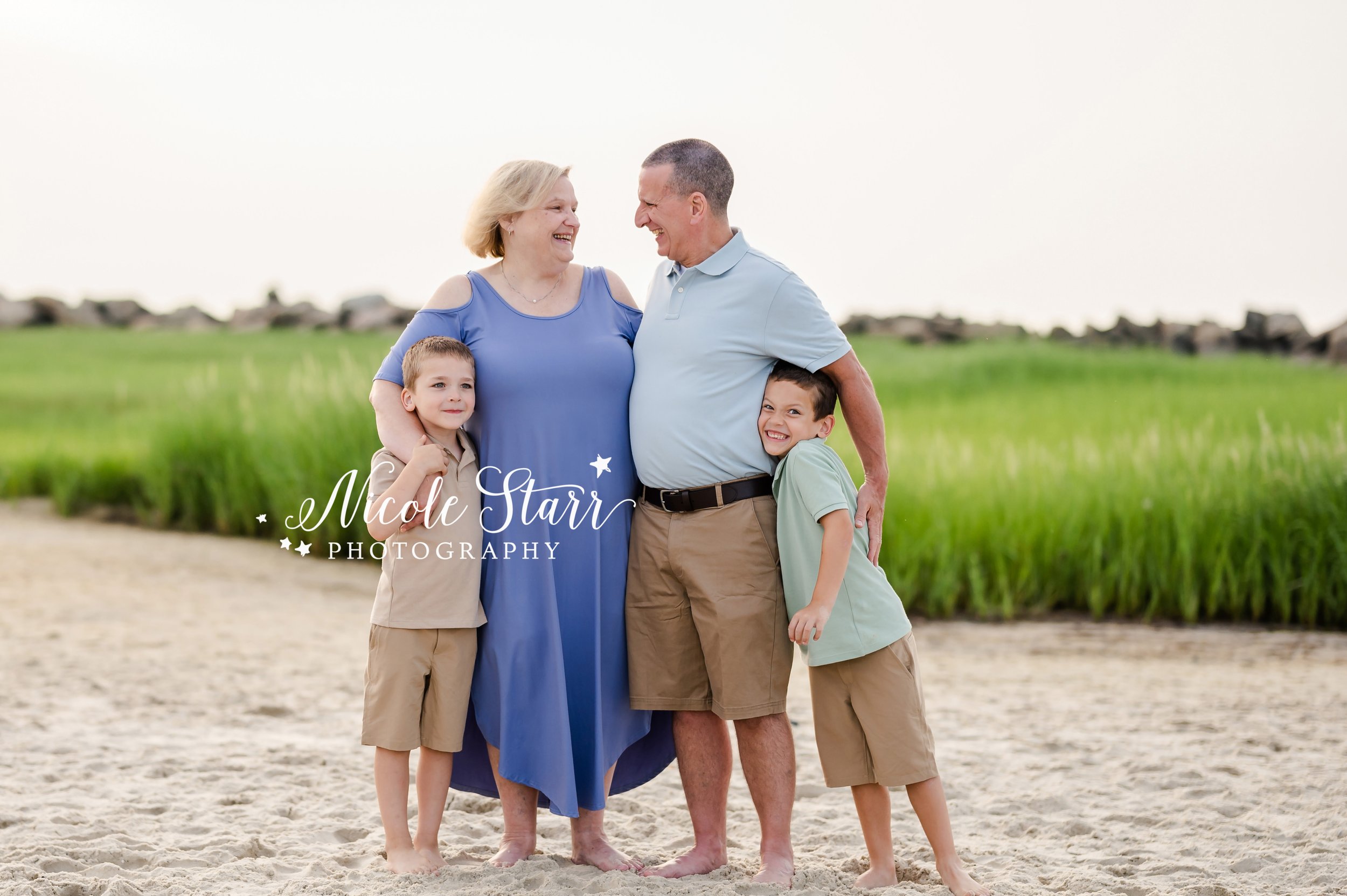 grandparents hug 2 grandsons in front of sea grass during summer Cape Cod extend family portraits with MA beach photographer Nicole Starr Photography