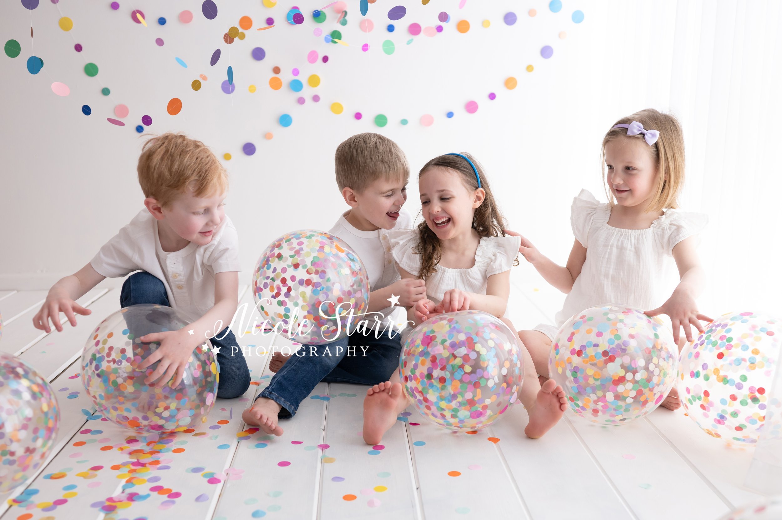 four toddlers play with confetti and beach balls in studio with rainbow streamers for cake smash with Nicole Starr Photography, Saratoga Springs children’s photographer