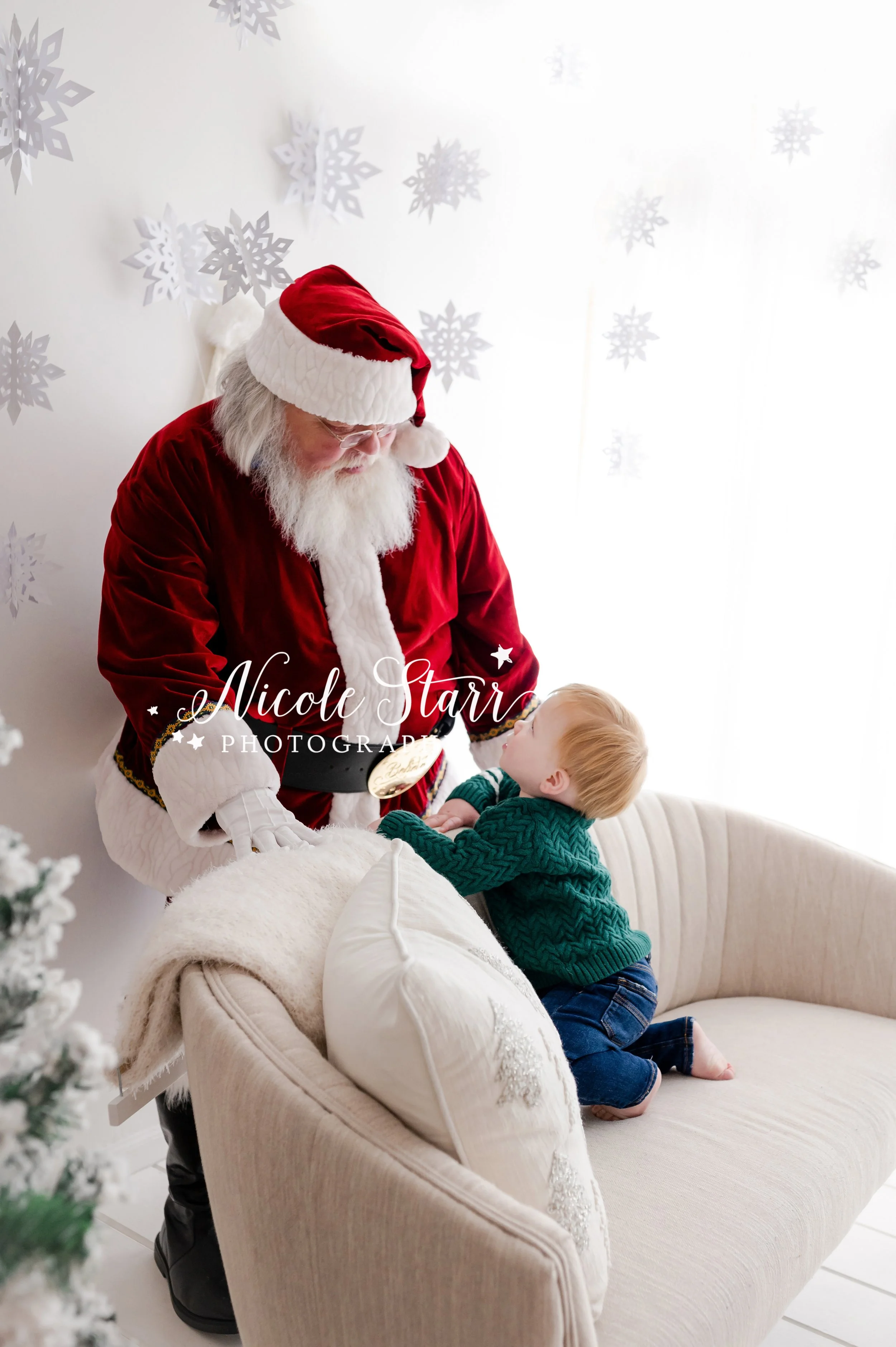baby boy in green sweater crawls on back of couch to reach Santa during Saratoga Springs holiday studio session with Santa Claus photographed by NY children’s photographer Nicole Starr Photography