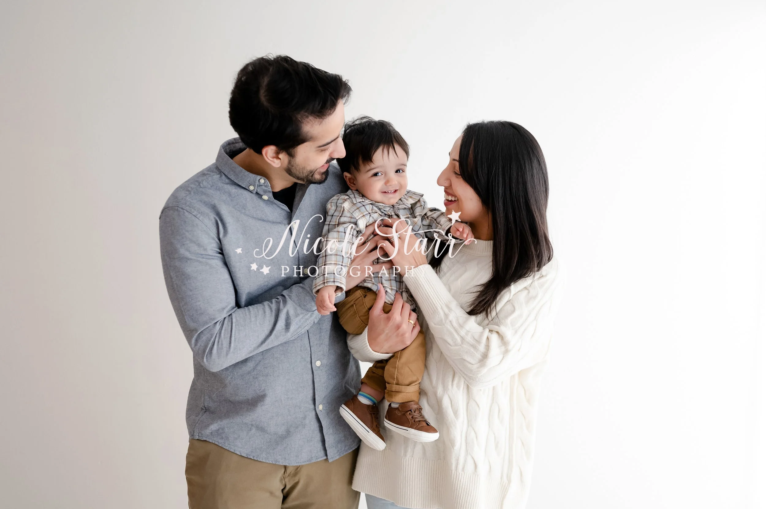 parents snuggle with one year old son between them in studio during first year birthday portraits with Saratoga Springs baby photographer Nicole Starr Photography