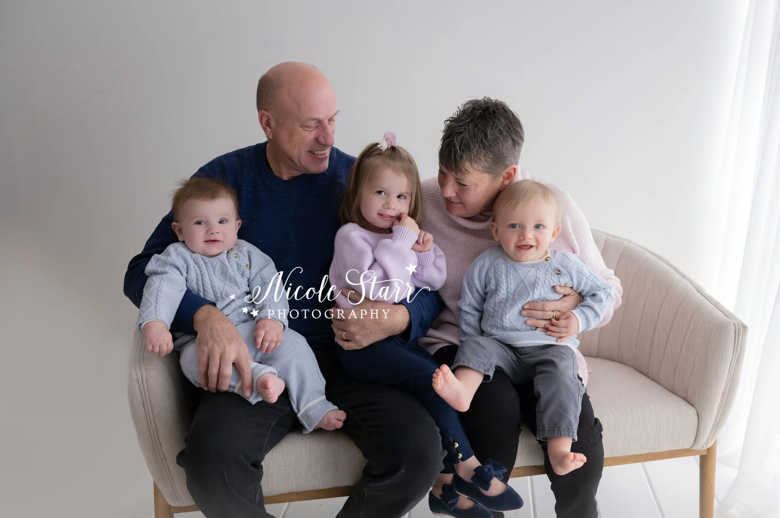 grandparents hold three grandkids in studio during family portraits with Nicole Starr Photography